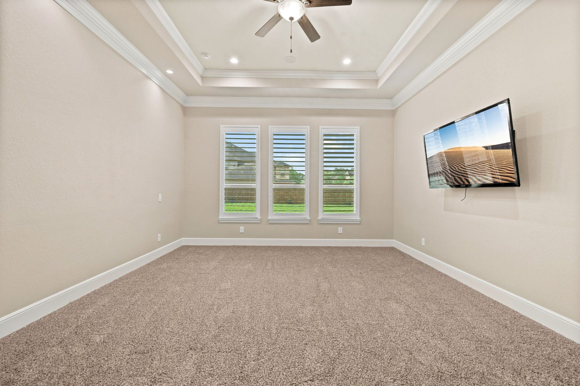 Primary bedroom showcasing a tray ceiling and has custom lighting and a ceiling fan.