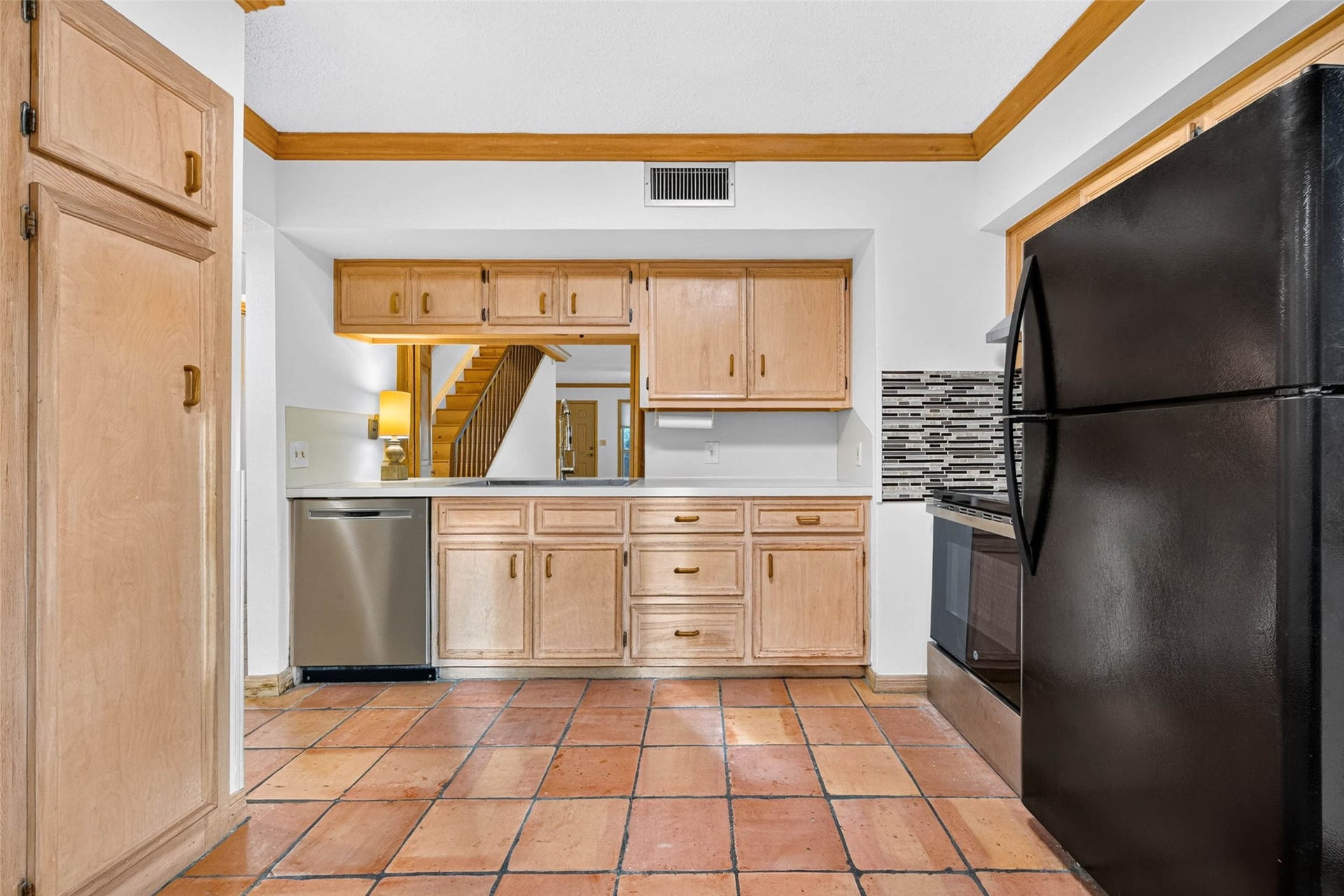 Charming kitchen featuring natural wood cabinets, a sleek black refrigerator, and modern appliances, complemented by a stylish tile backsplash and warm flooring.