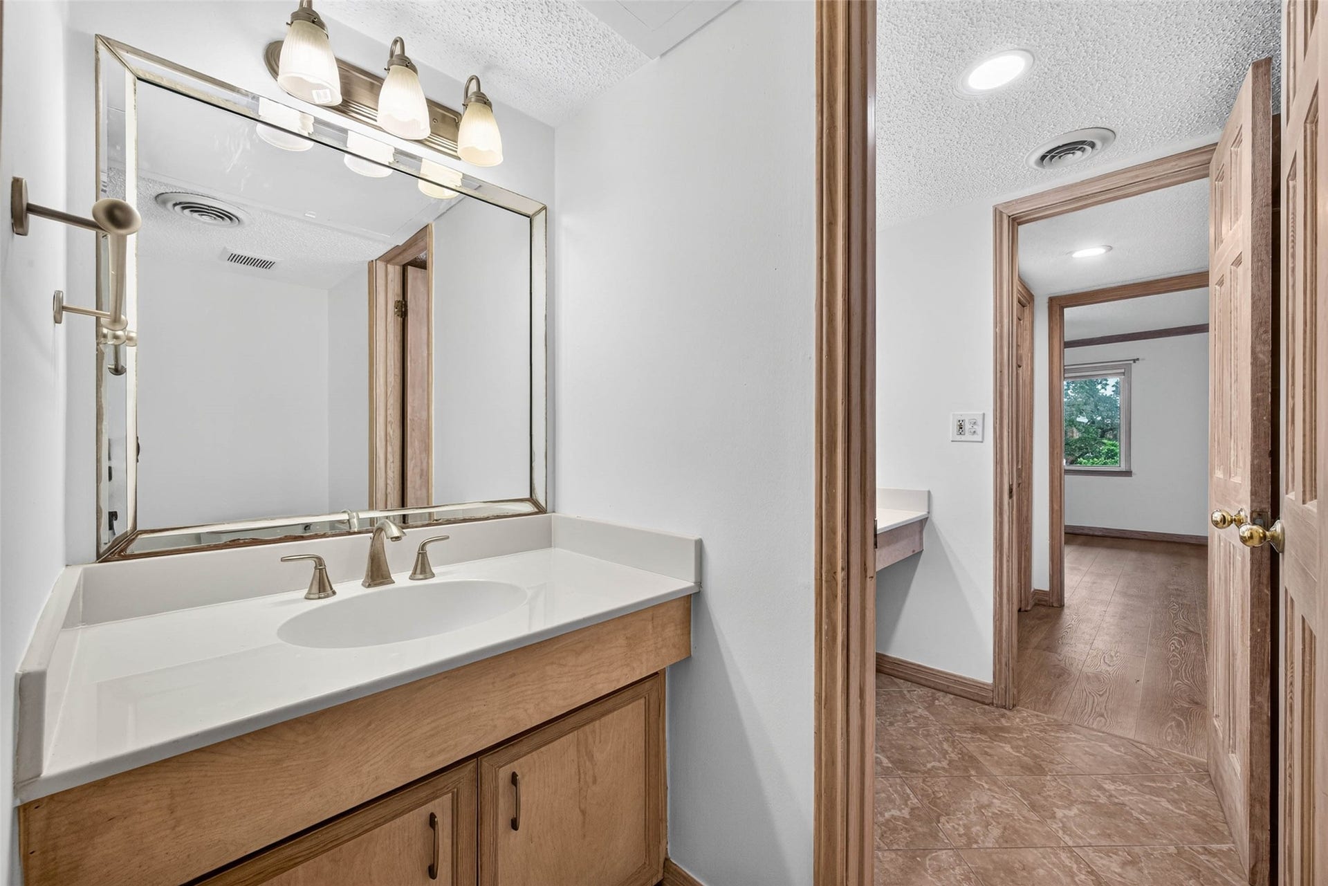 Elegant bathroom with a spacious vanity, large mirror, and modern lighting, leading to a cozy hallway with warm wood accents and natural light.