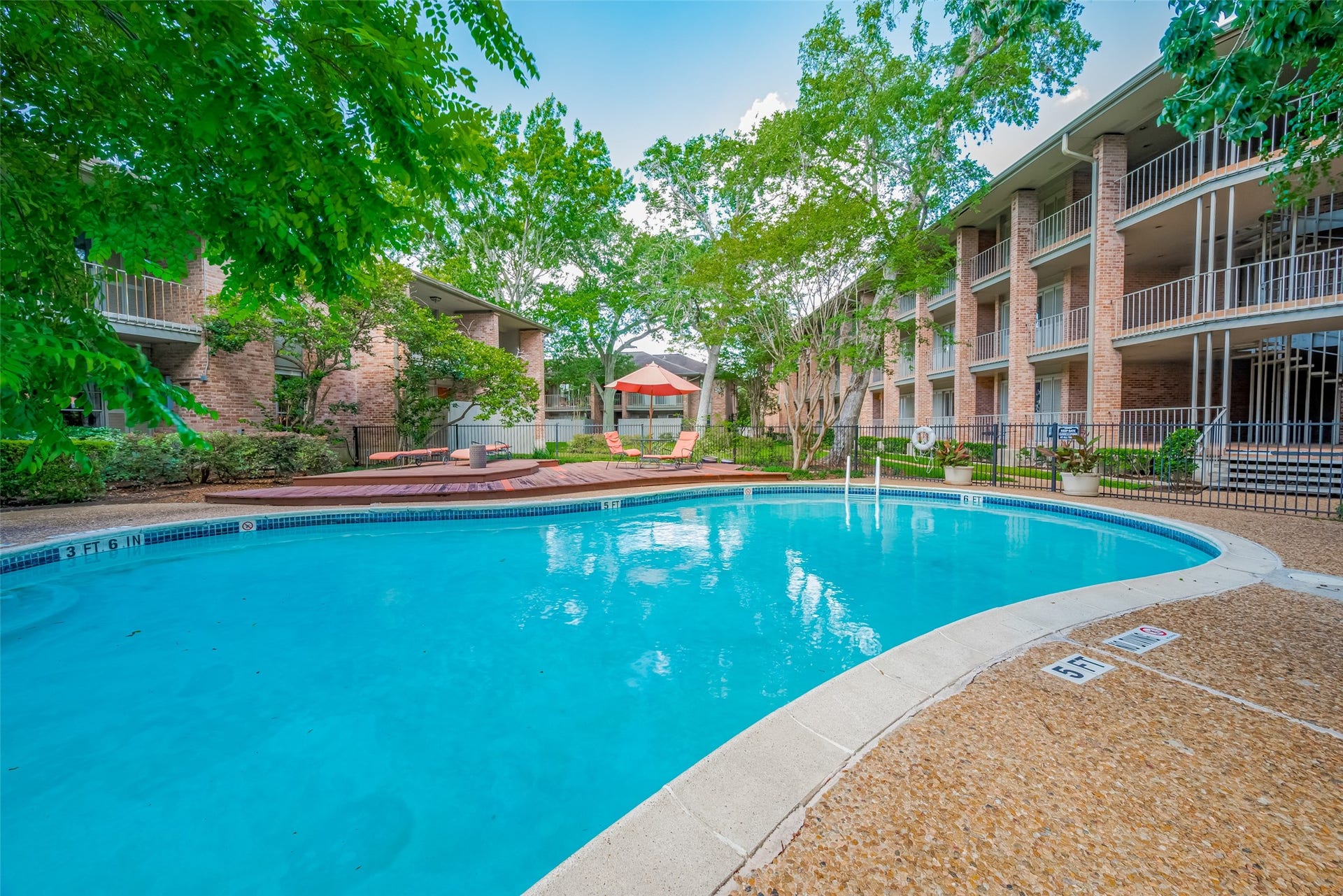 Experience serene living with this inviting courtyard pool, surrounded by lush greenery and well-maintained brick apartment buildings, perfect for relaxation and leisure.