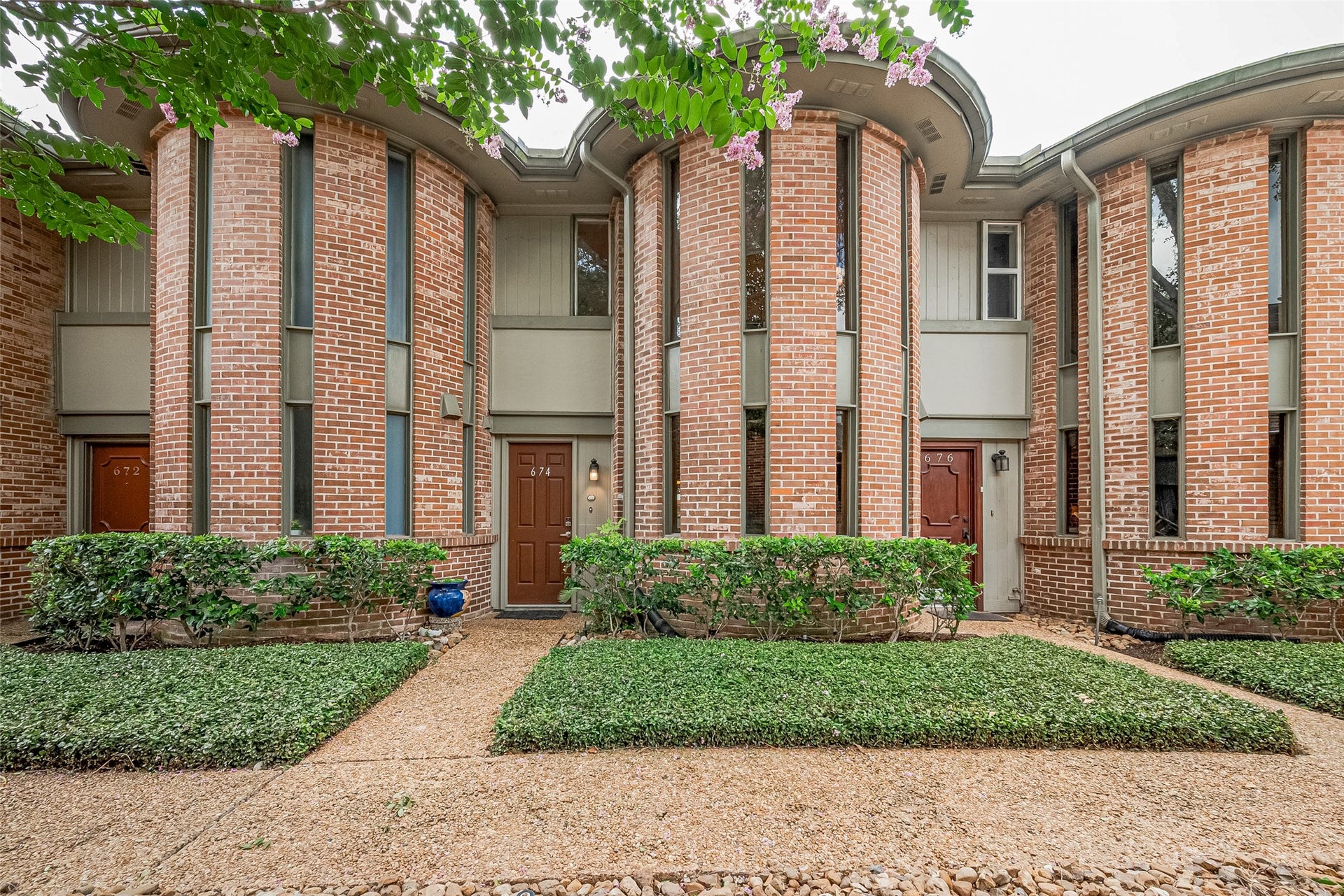 Charming brick townhouse with distinctive curved architecture and lush landscaping, offering a welcoming entrance.