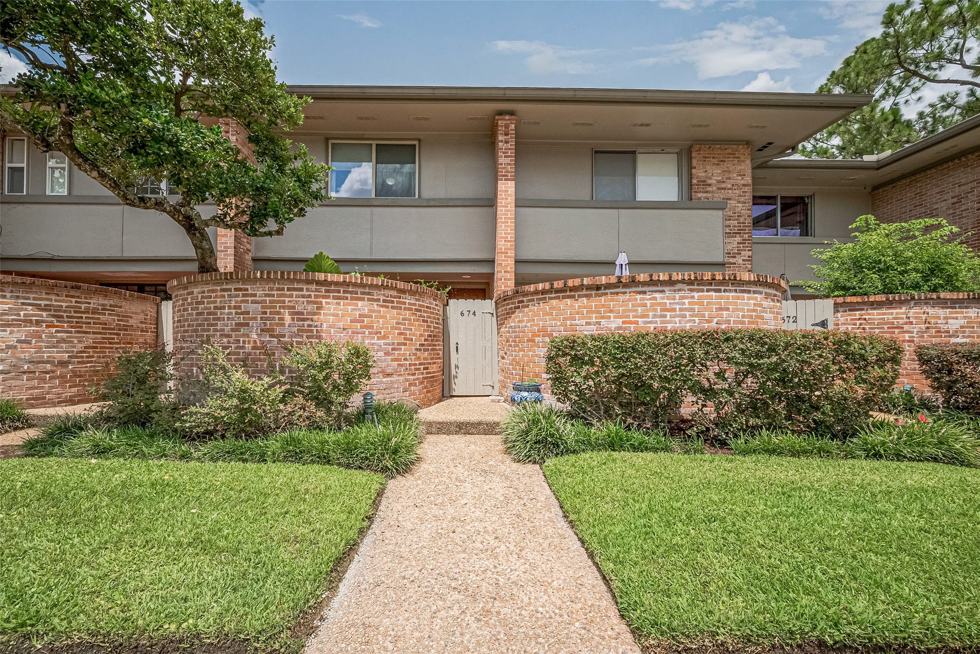 Charming two-story townhouse with a classic brick exterior and private gated entrance, surrounded by lush landscaping and mature trees.
