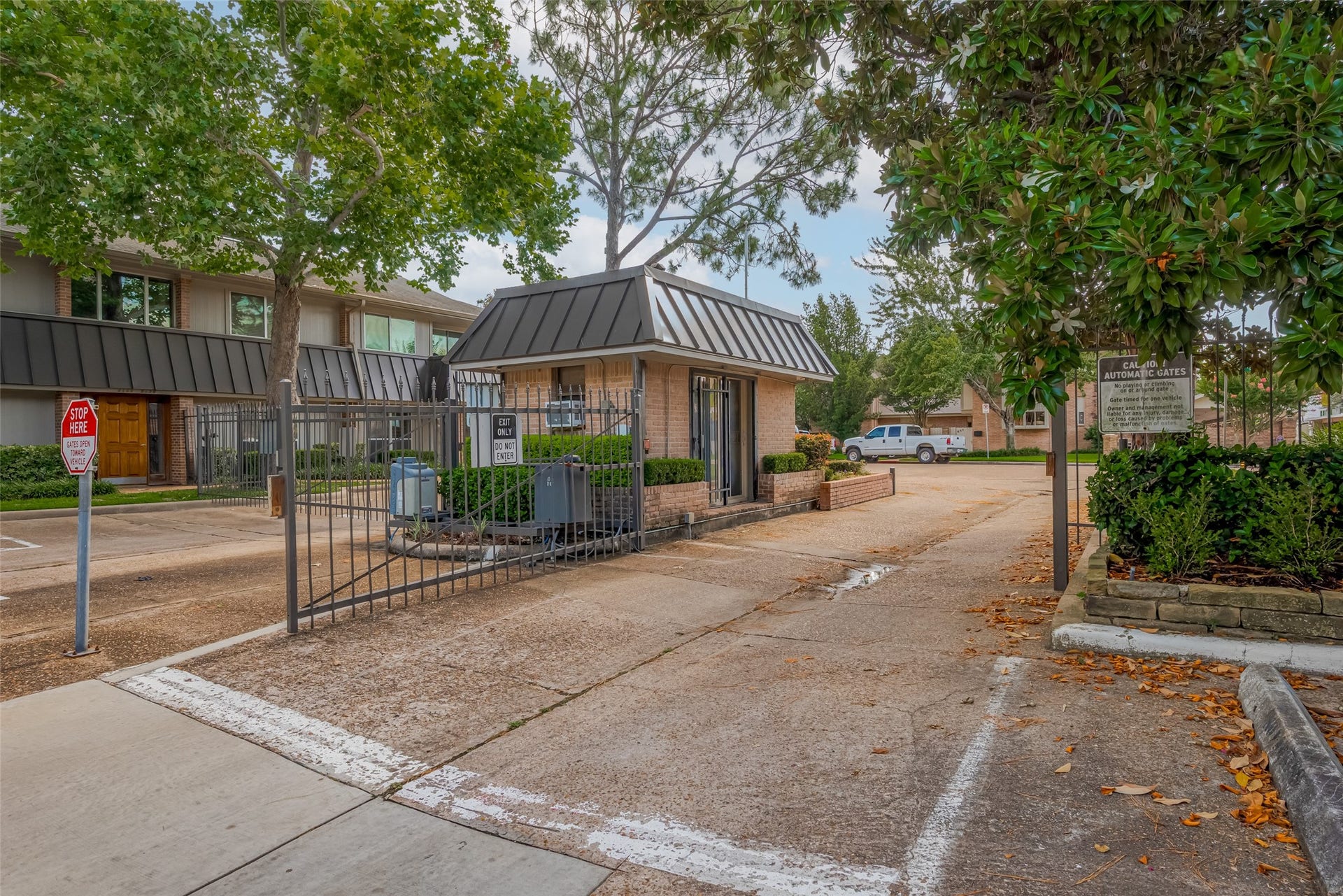 Charming gated community entrance with lush greenery and ample parking, offering security and privacy for residents.