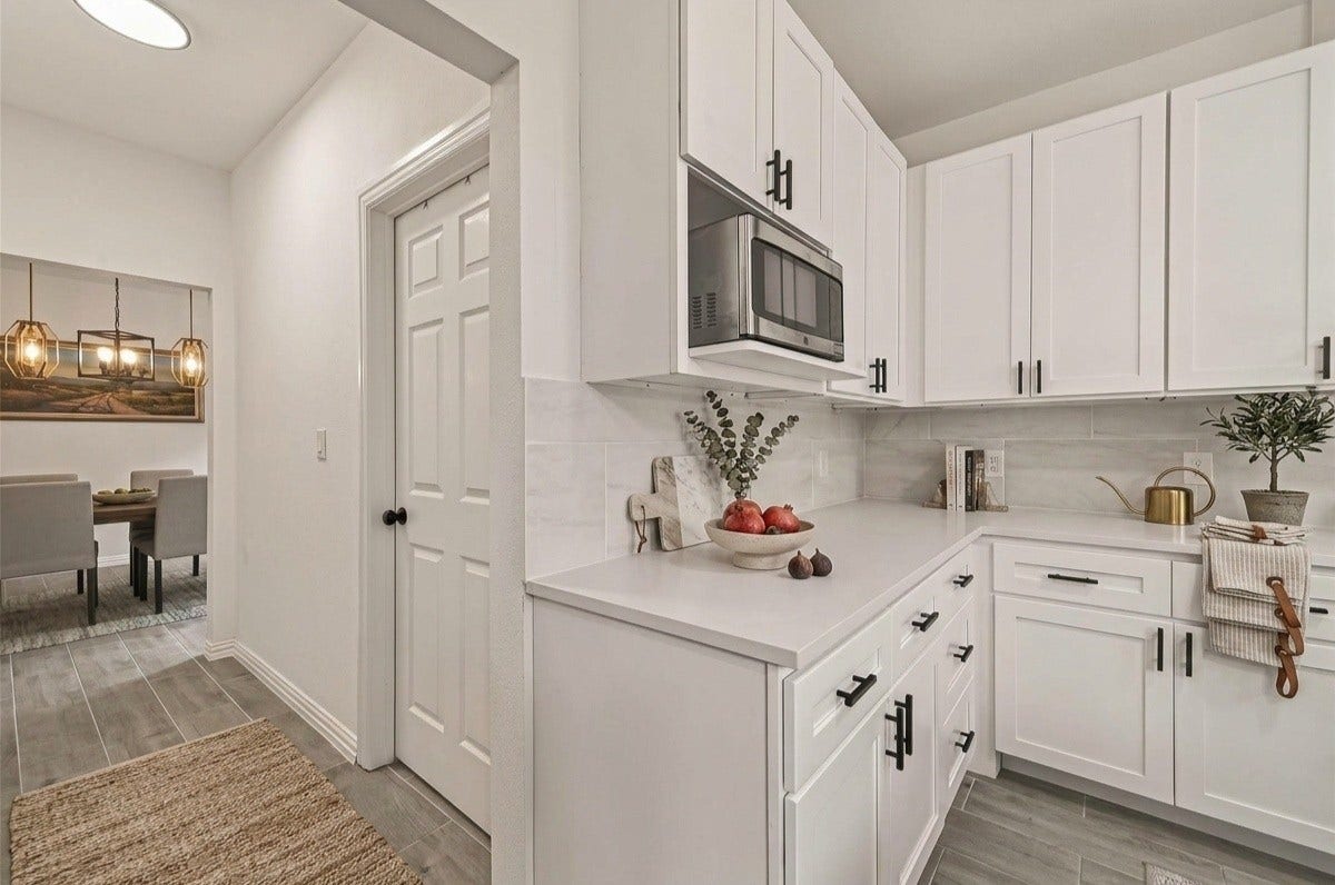 4423 Parkwater Cove Court SE, Sugar Land, TX 77479 This photo showcases a modern kitchen with sleek white cabinetry, black hardware, and a built-in microwave. The space is bright with neutral tile flooring and a view into a dining area with a stylish pendant light