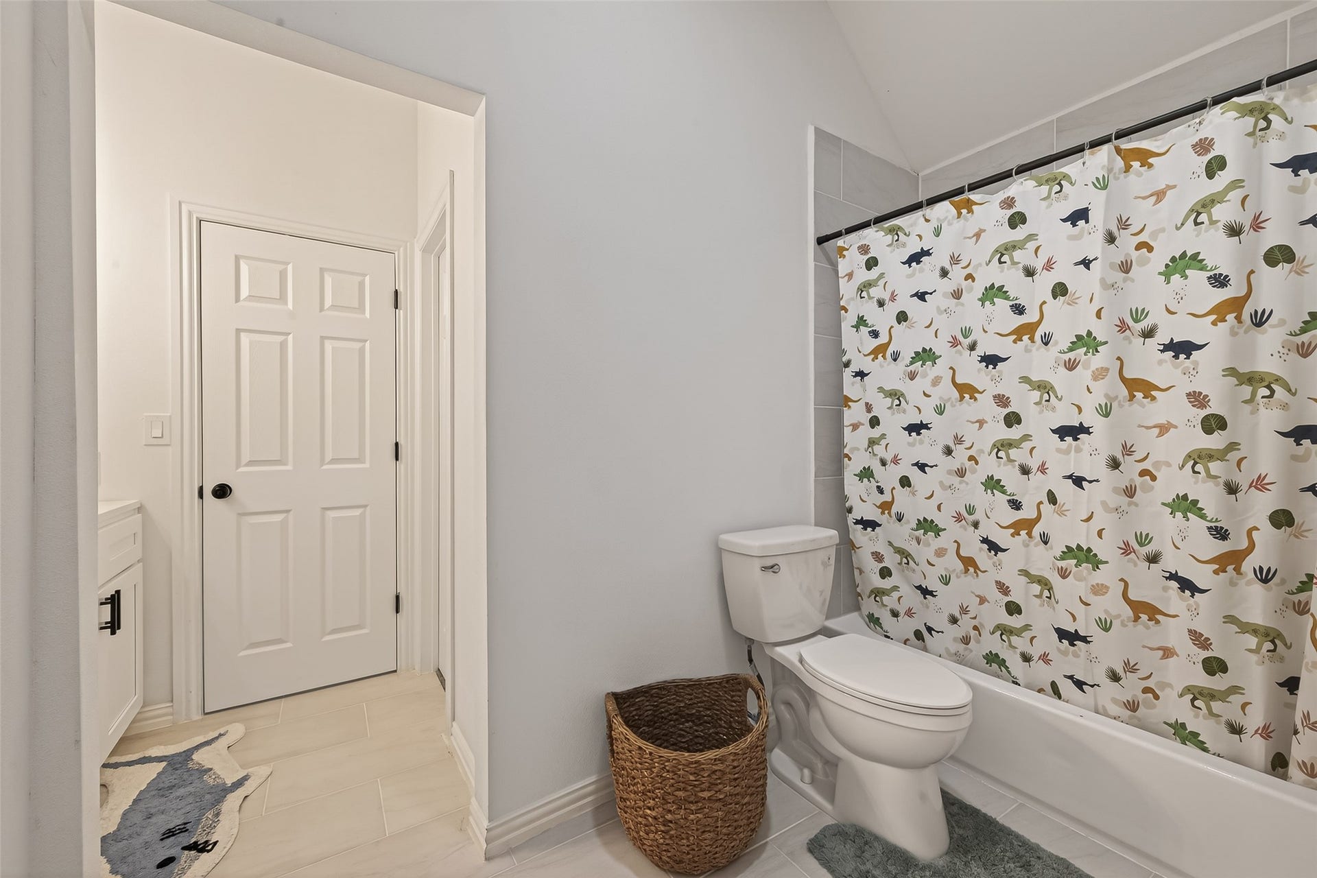 4423 Parkwater Cove Court SE, Sugar Land, TX 77479 This bathroom features a clean white aesthetic with a playful dinosaur-themed shower curtain. It includes a bathtub, toilet, with tile flooring and a door leading to a vanity space.