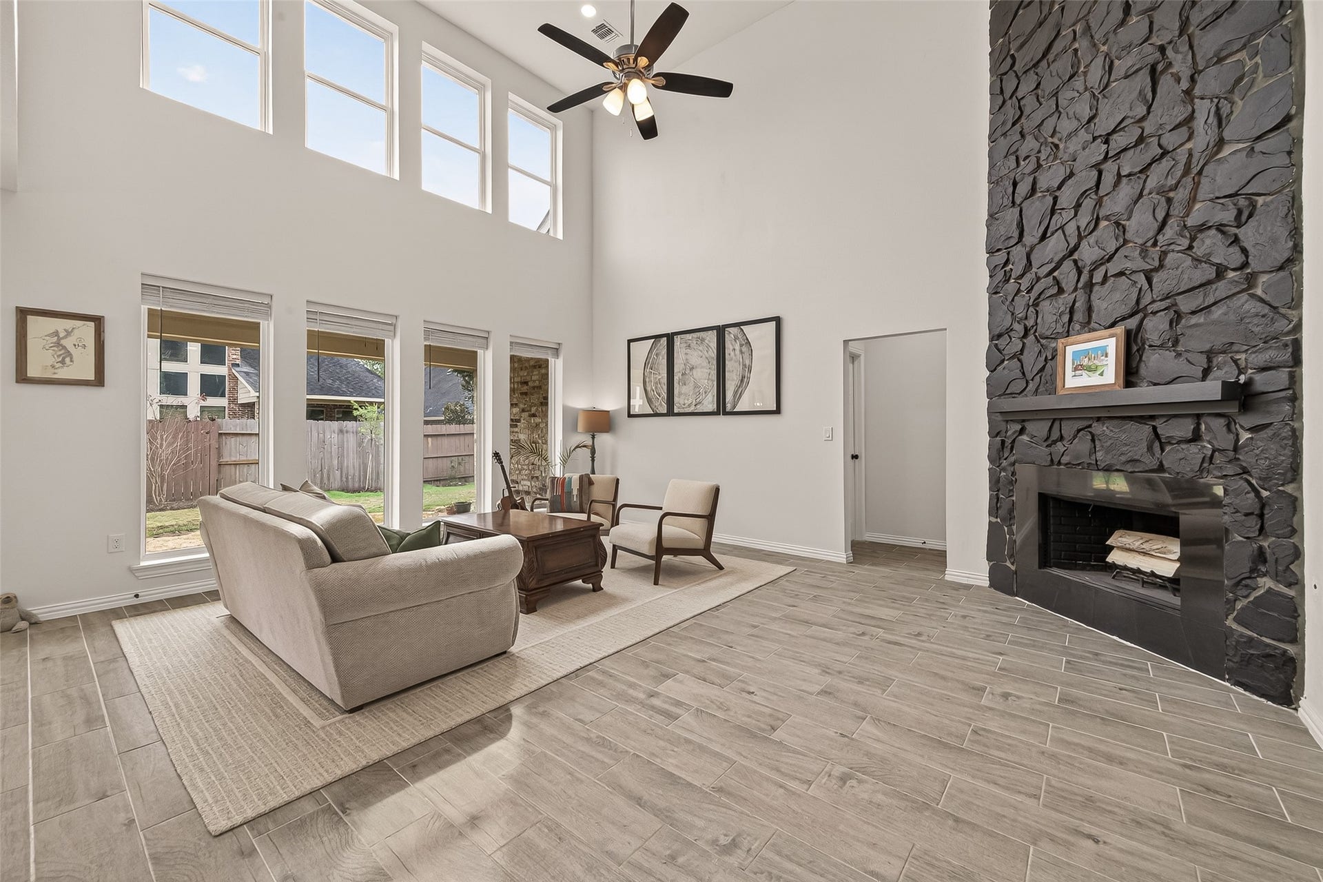 4423 Parkwater Cove Court SE, Sugar Land, TX 77479 This spacious living room features a high ceiling with ample natural light from large windows. It includes a striking stone fireplace, wood flooring, and a cozy seating area. The open layout offers a welcoming and comfortable atmosphere.