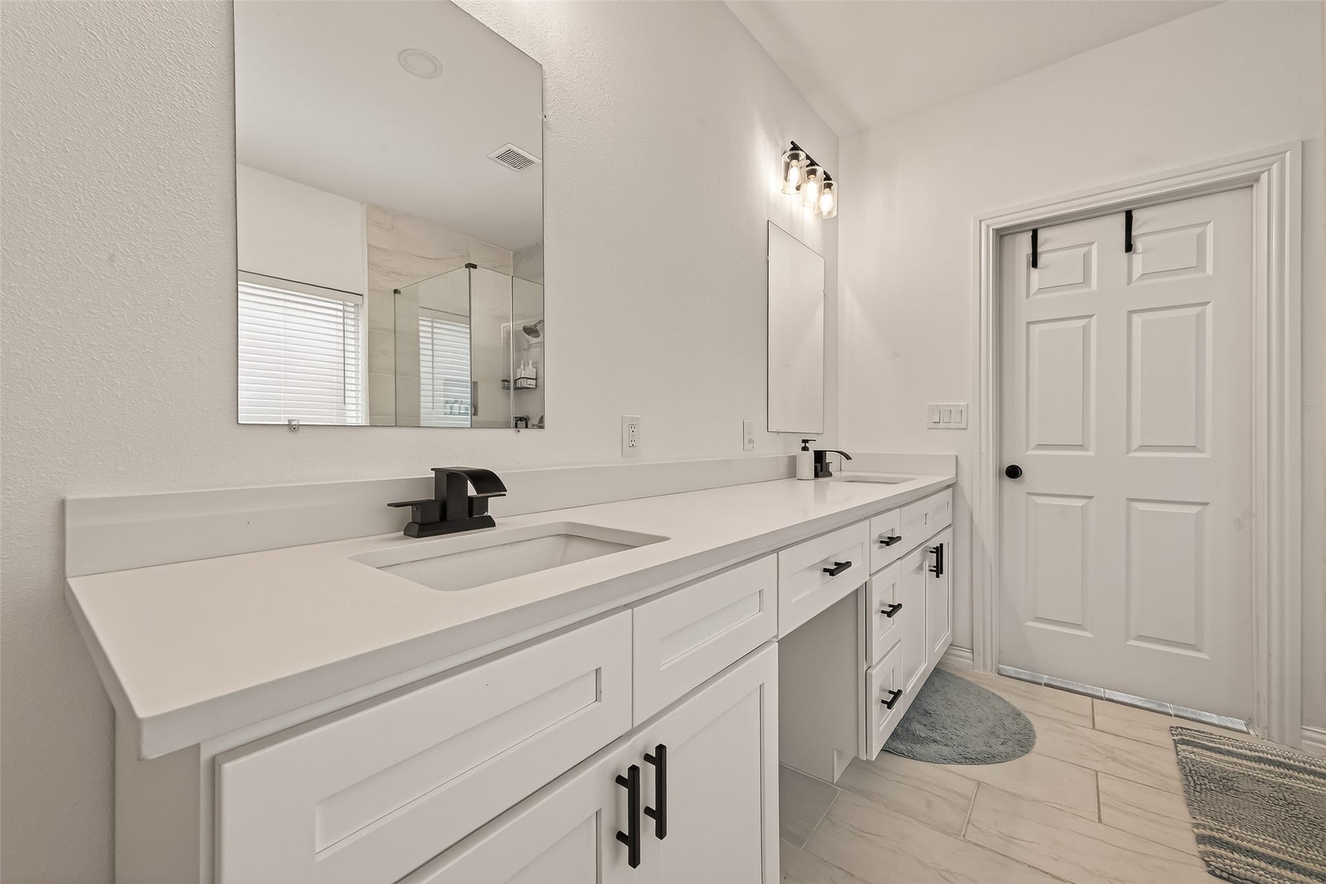4423 Parkwater Cove Court SE, Sugar Land, TX 77479 This modern bathroom features a long double vanity with sleek black fixtures, ample storage, and two mirrors. The space is bright and airy with light-colored tiles and a glass-enclosed shower.