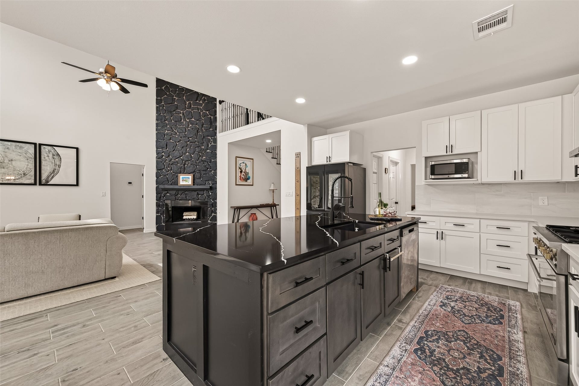 4423 Parkwater Cove Court SE, Sugar Land, TX 77479 This photo showcases a modern open-concept kitchen and living area. It features a large island with a sleek black countertop, stainless steel appliances, and white cabinetry. The living area has a cozy feel with a stone accent wall and a ceiling fan, providing a stylish and functional space.