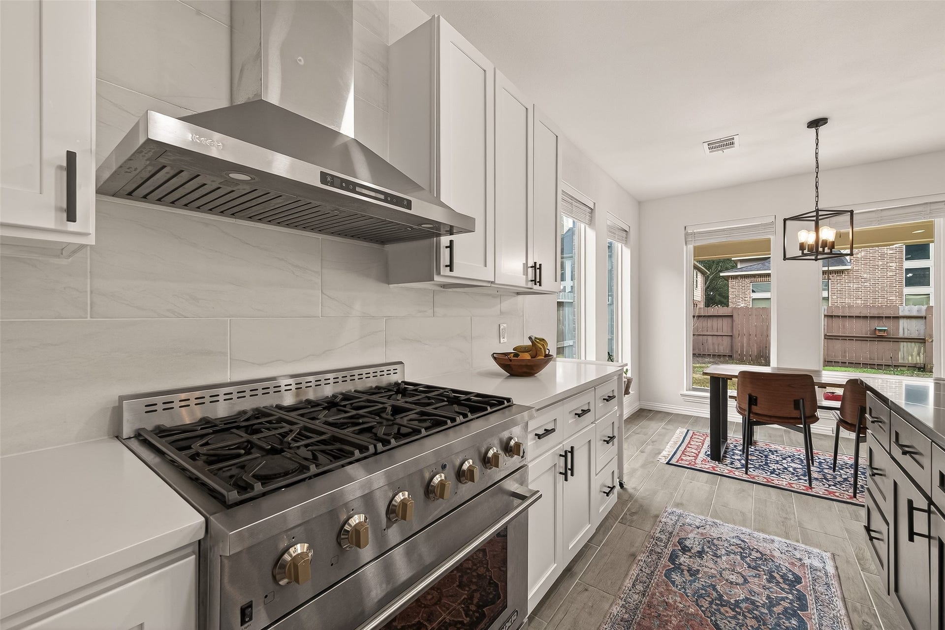 4423 Parkwater Cove Court SE, Sugar Land, TX 77479 This kitchen features modern stainless steel appliances, including a gas range with a sleek hood. It has white cabinetry, a neutral tile backsplash, and an open dining area with large windows that provide ample natural light and a view of the backyard.