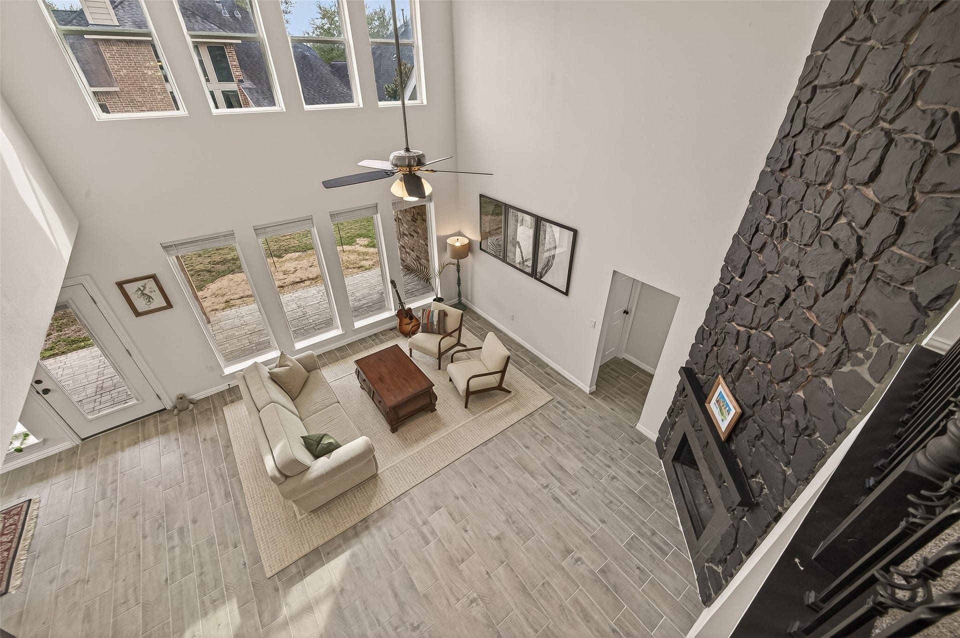 4423 Parkwater Cove Court SE, Sugar Land, TX 77479 This photo showcases a spacious, modern living room with high ceilings and abundant natural light from large windows. It features a cozy seating area, a stone accent wall with a fireplace, and light wood flooring. The neutral color palette adds to the room's airy feel.