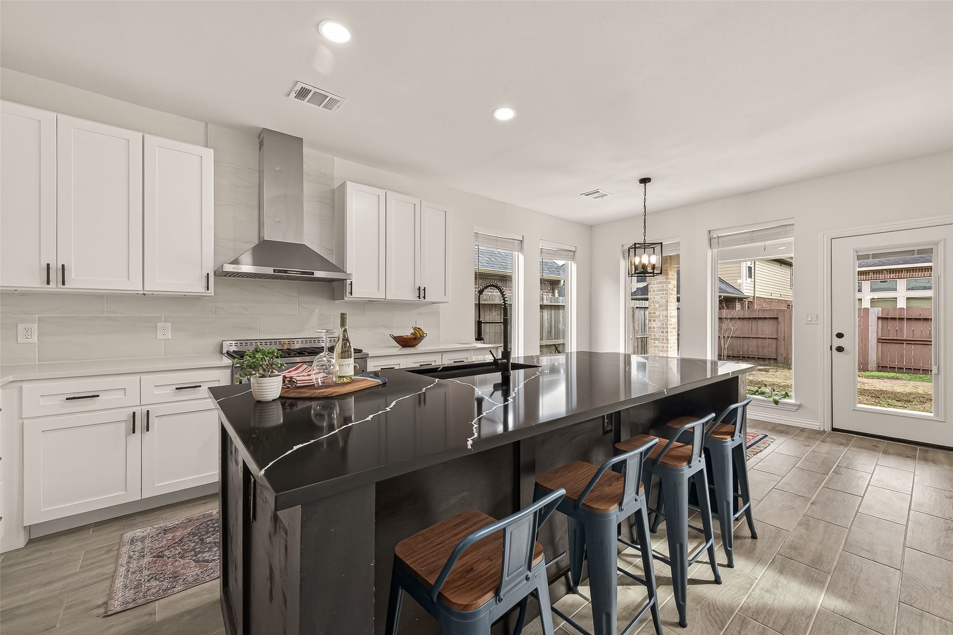 4423 Parkwater Cove Court SE, Sugar Land, TX 77479 This modern kitchen features sleek white cabinetry, a large black island with seating, stainless steel appliances, and ample natural light from multiple windows and a glass door leading to the backyard.