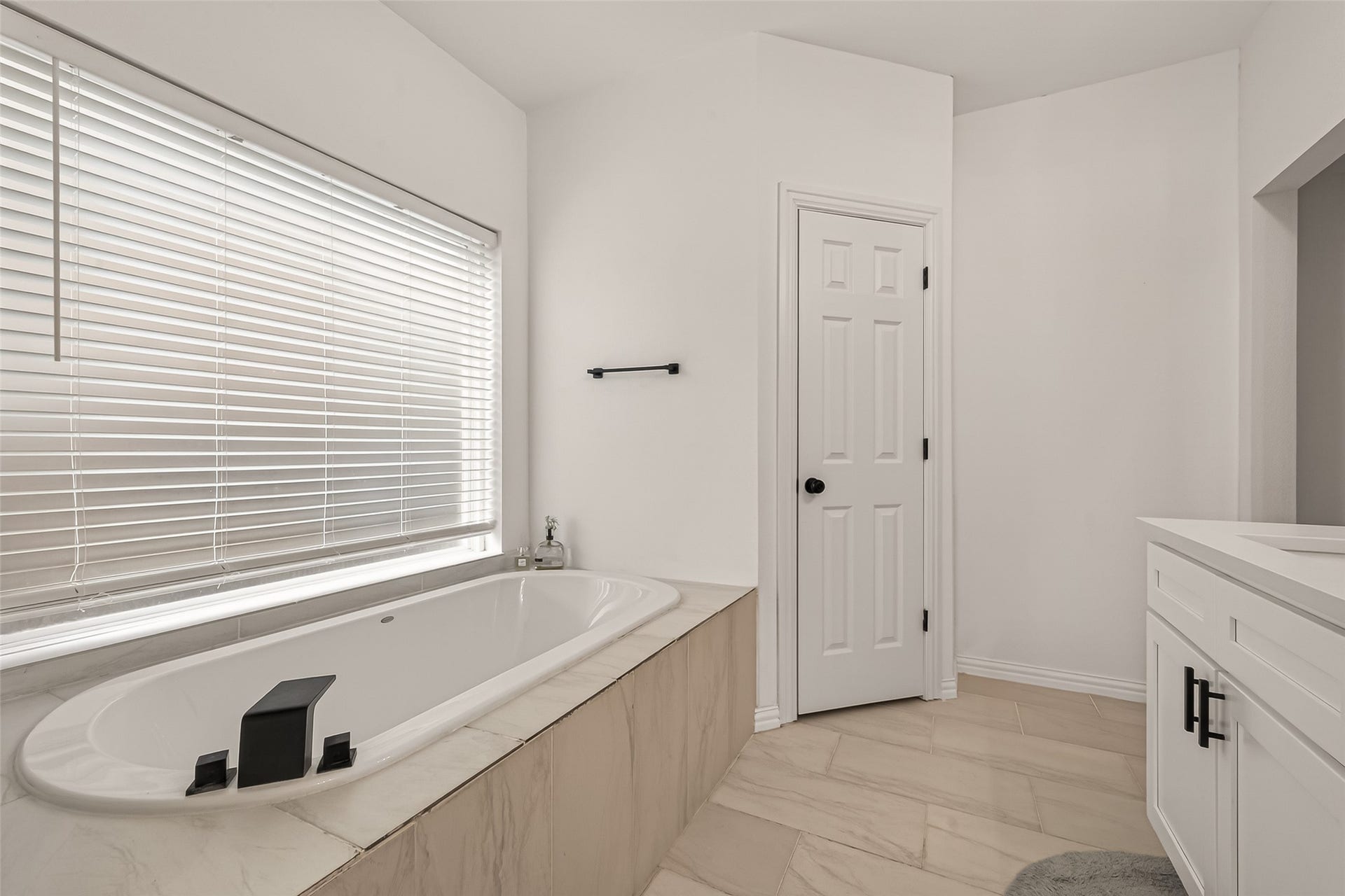 4423 Parkwater Cove Court SE, Sugar Land, TX 77479 This bathroom features a modern soaking tub with sleek fixtures, a large window with blinds, and a door leading to additional space. The bright, neutral design is complemented by a stylish vanity and light tile flooring.
