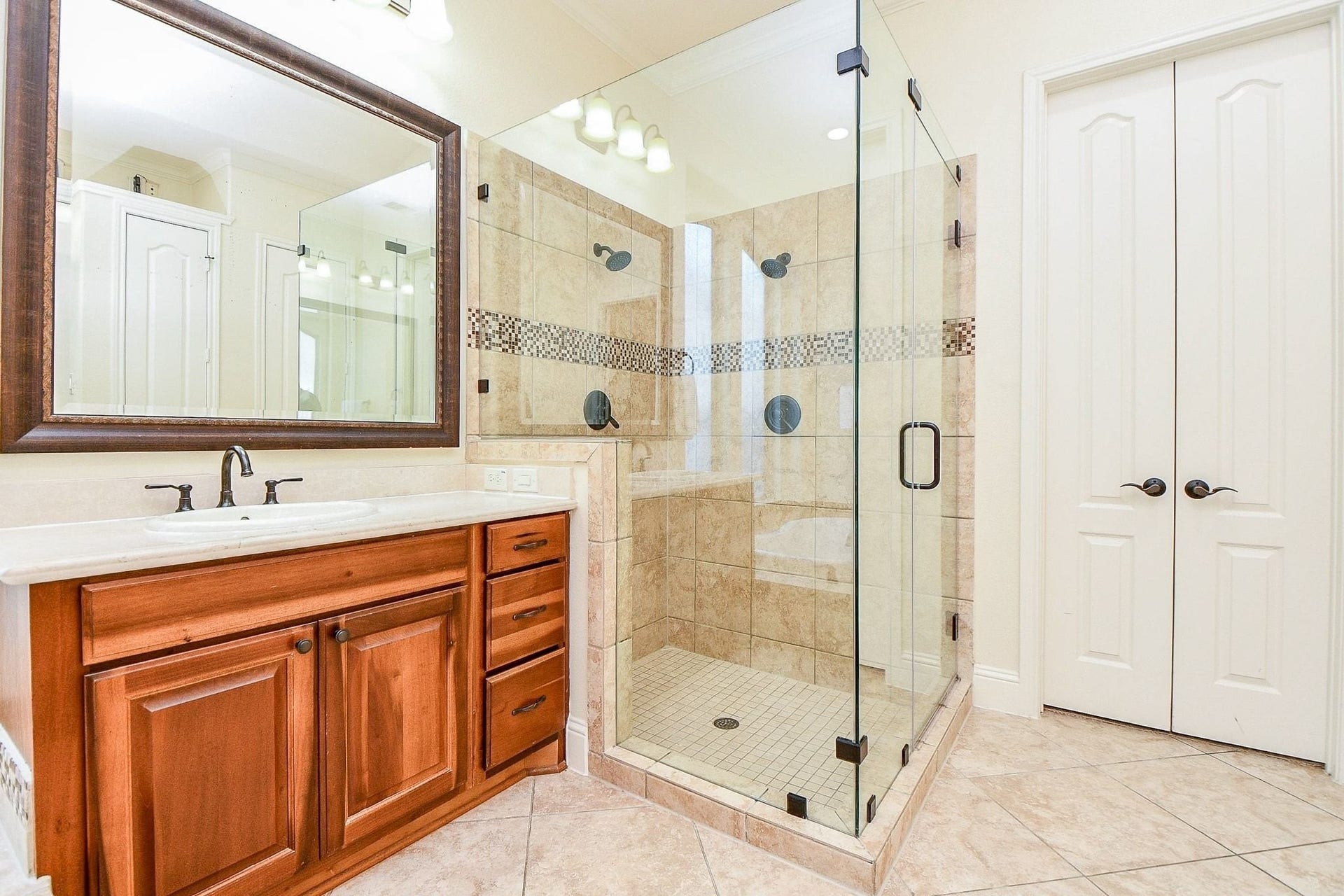 11410 Sardinia Drive, Richmond, TX 77406 A closer look at the beautiful walk-in shower featuring tiled flooring and a decorative tile surround, complemented by an elegant framed mirror and beautifully coordinated cabinetry and countertops.