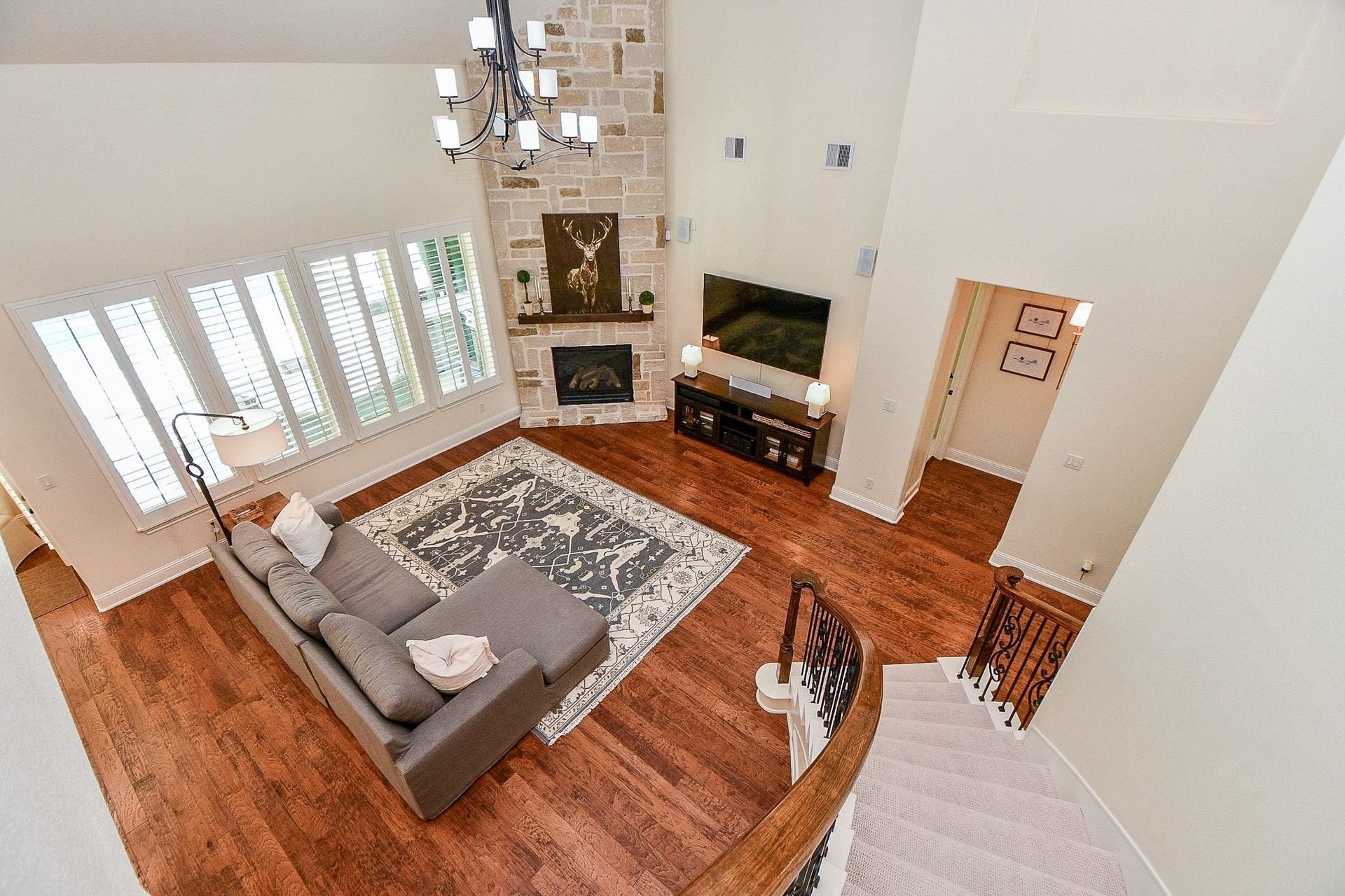 11410 Sardinia Drive, Richmond, TX 77406 This view truly captures the grandeur of the living room, featuring a stunning floor-to-ceiling stone gas-log fireplace and an elegant lighting fixture that beautifully complements the curved wrought-iron staircase.