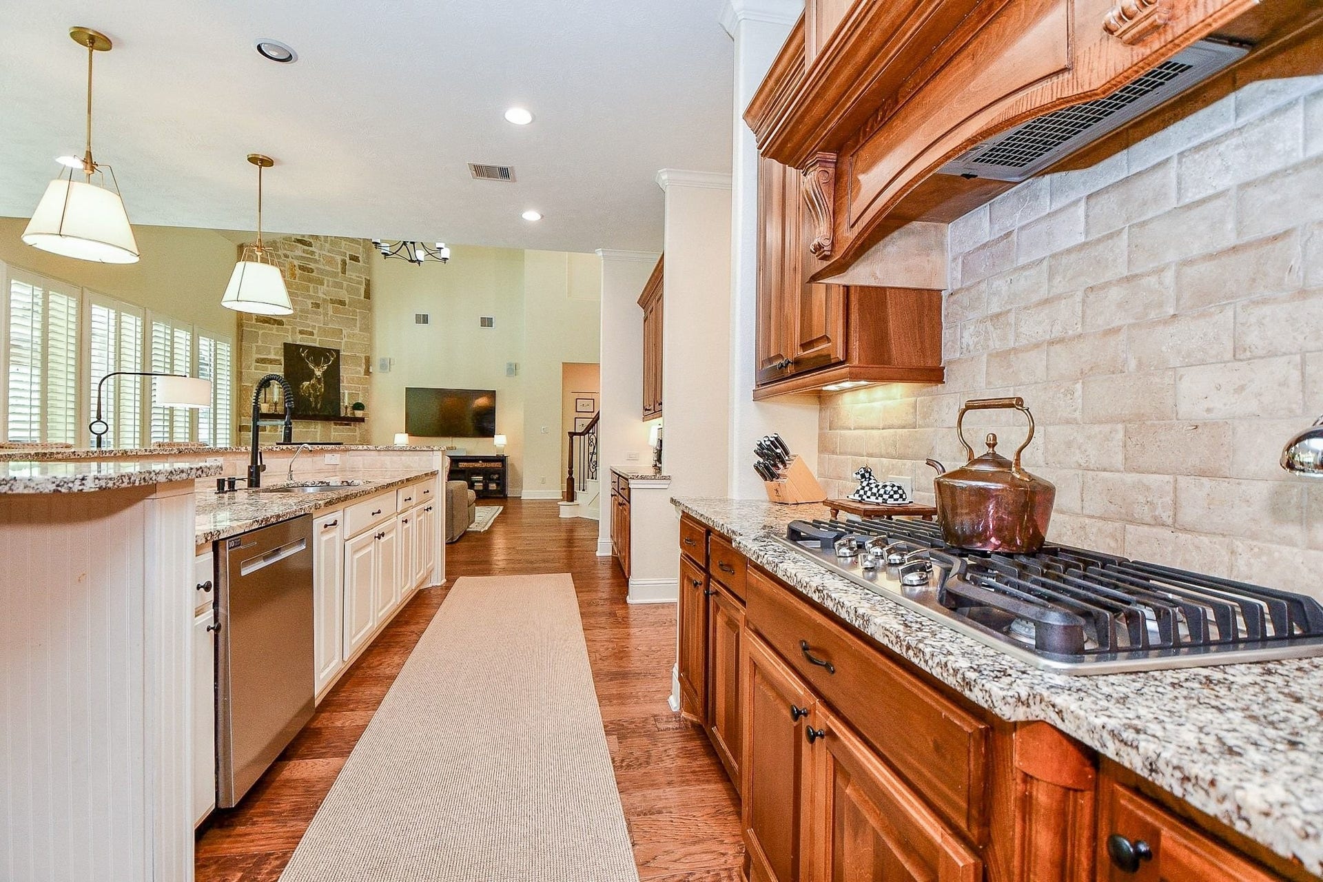 11410 Sardinia Drive, Richmond, TX 77406 A closer look highlights the 5-burner gas cooktop, elegant tile backsplash, and beautifully coordinated granite countertops. Under-cabinet lighting and intricate wood cabinetry details add warmth, character, and an unmistakable touch of luxury.