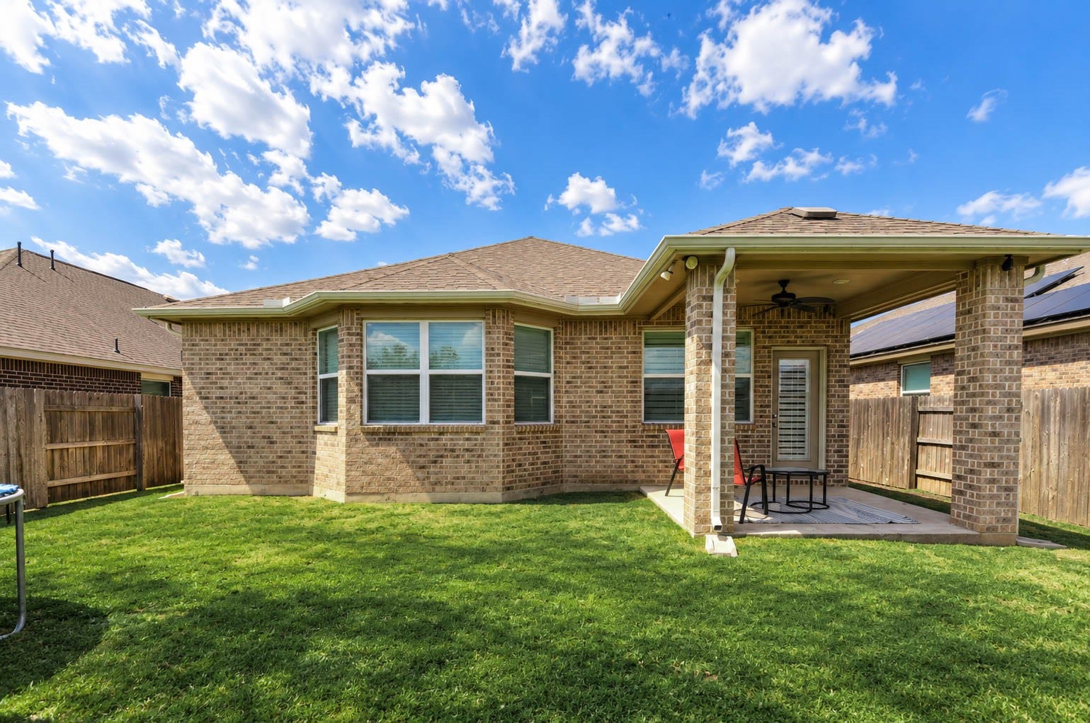 Daytime backyard view highlighting the covered patio, green lawn, and space for outdoor enjoyment.