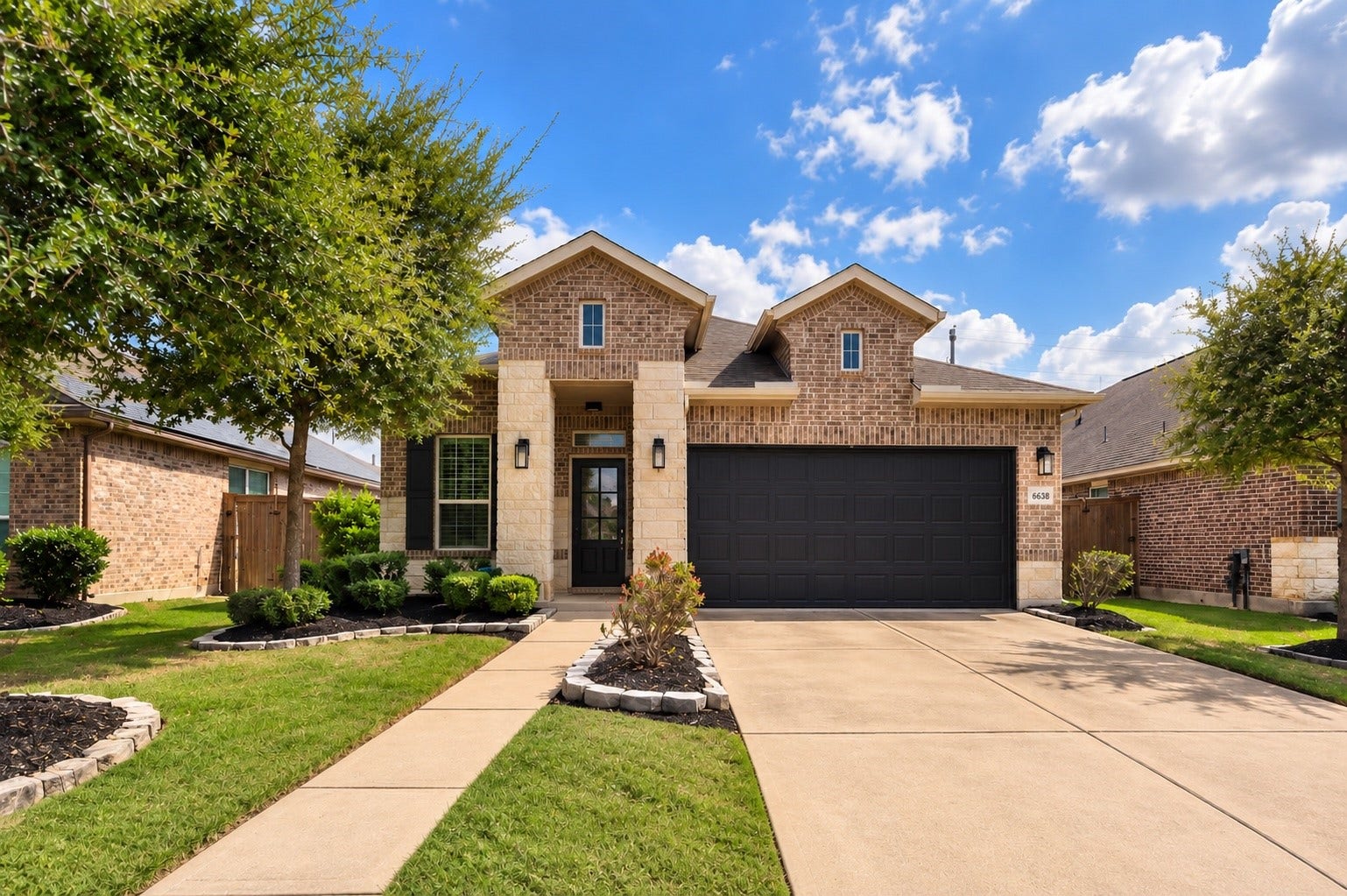 Welcoming front elevation featuring attractive brick and stone accents, a two-car garage, and a landscaped front yard.