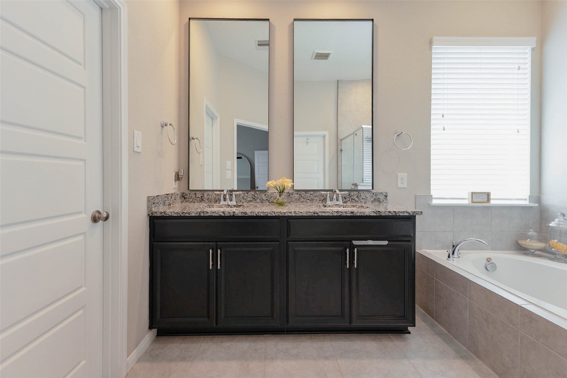 Primary bathroom featuring a double-sink vanity with dark cabinetry, framed mirrors, and a soaking tub.
