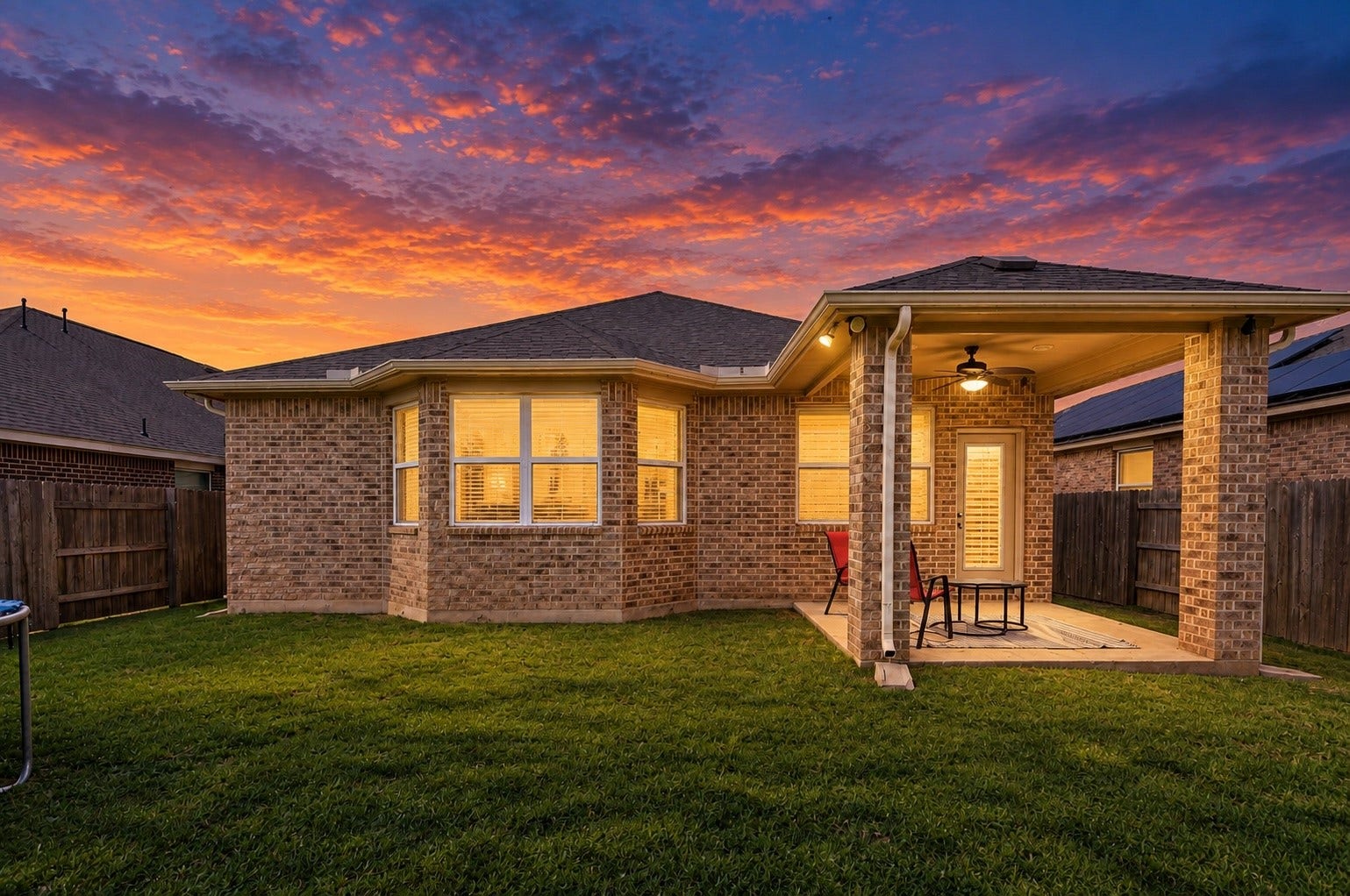 Stunning twilight view of the backyard featuring a covered patio, spacious lawn, and beautiful evening sky.