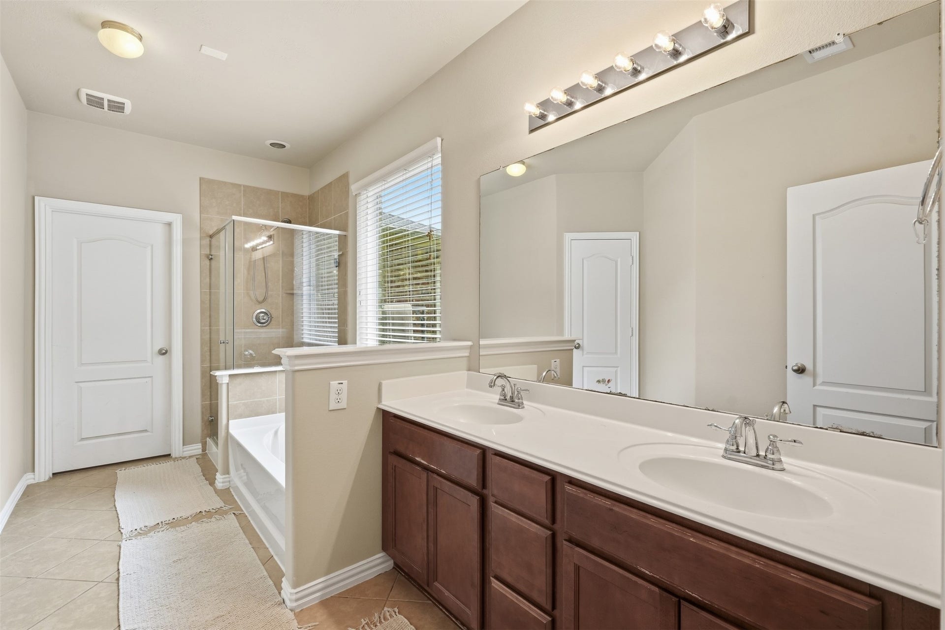 A primary bath with spa-day energy: double-sink vanity, oversized mirror, garden soaking tub and a separate glass-enclosed shower.