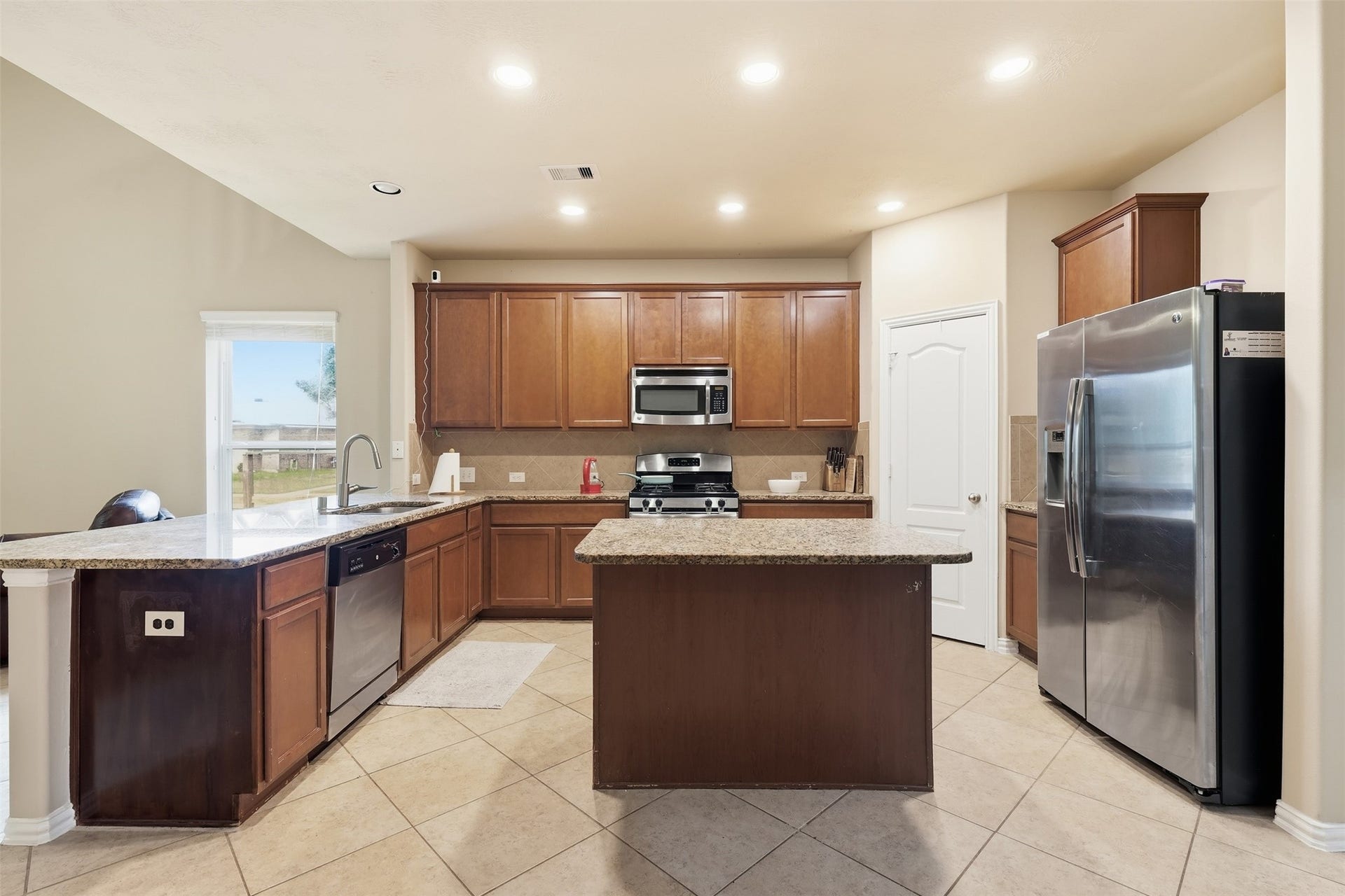 Chef's-eye view: wraparound granite with breakfast-bar seating, a walk-in pantry, generous cabinetry and a stainless dishwasher, plus a sunny window by the breakfast area.