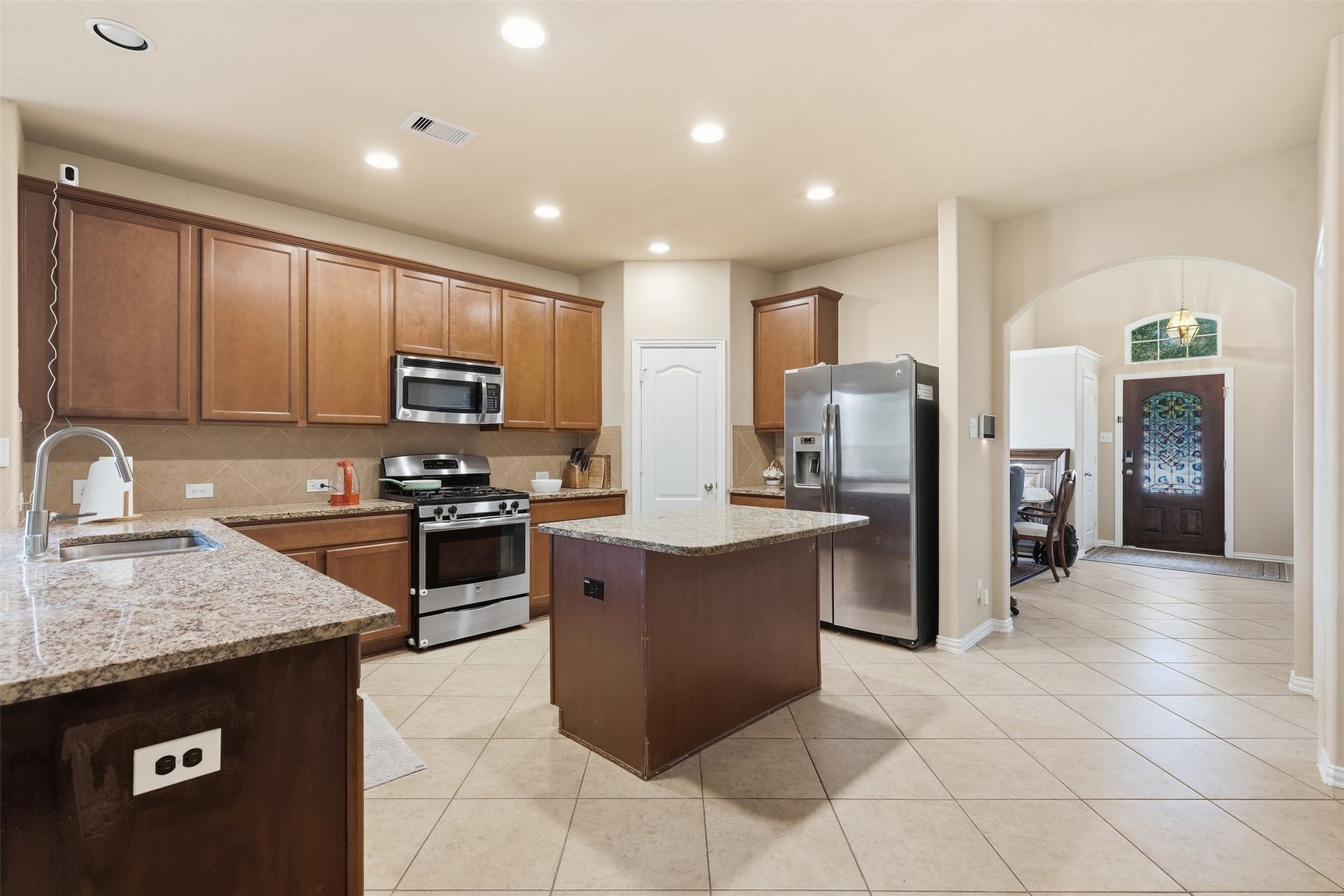 The kitchen everyone ends up in. Granite counters, a center island, gas range, stainless appliances, tile backsplash and recessed lighting, open to the dining area and entry.