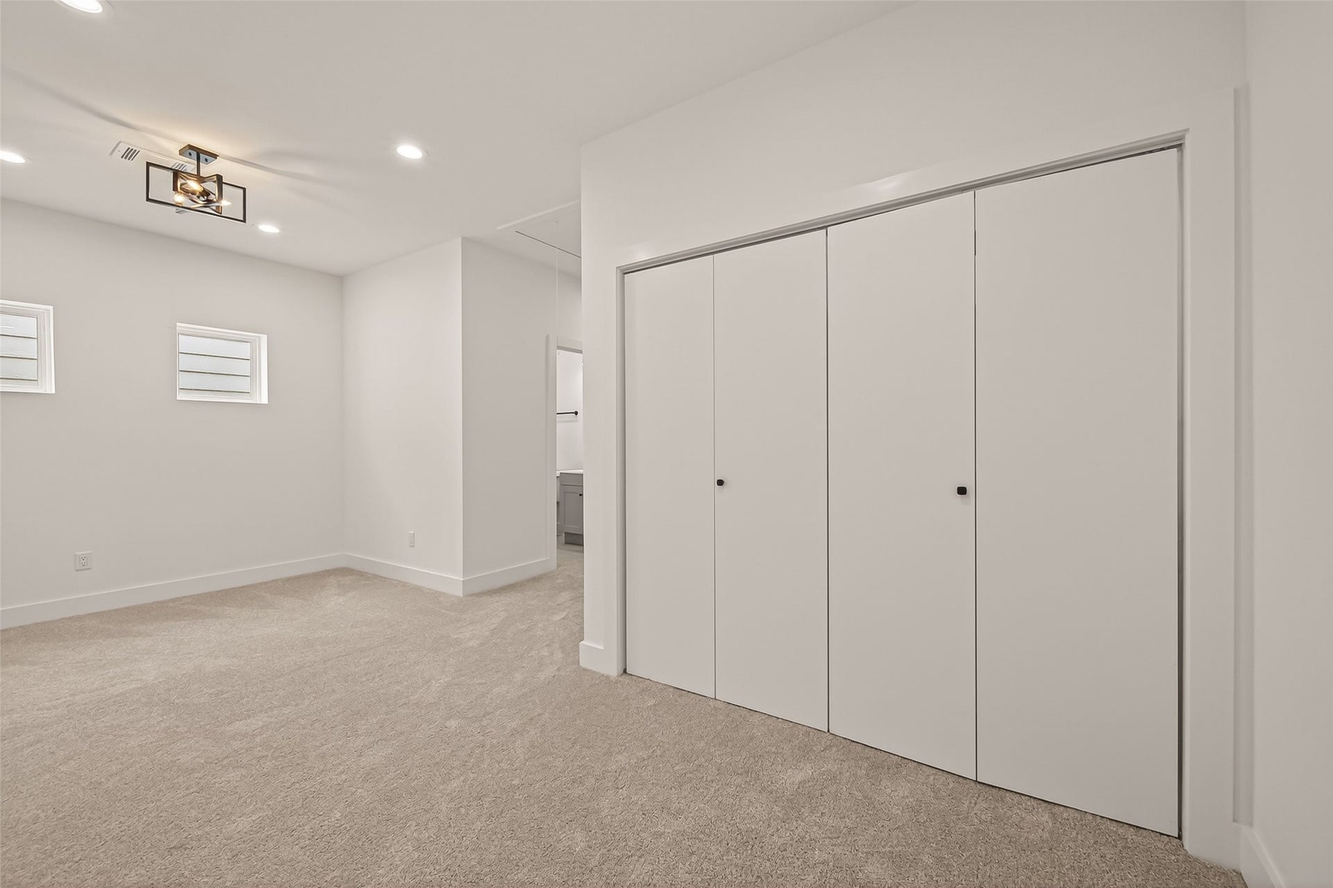 6808 Madrid Street, Houston, TX 77021 This photo showcases a spacious, modern bedroom with neutral carpet, ample closet space, and contemporary lighting. The room has a clean, minimalist design with two small windows for natural light.