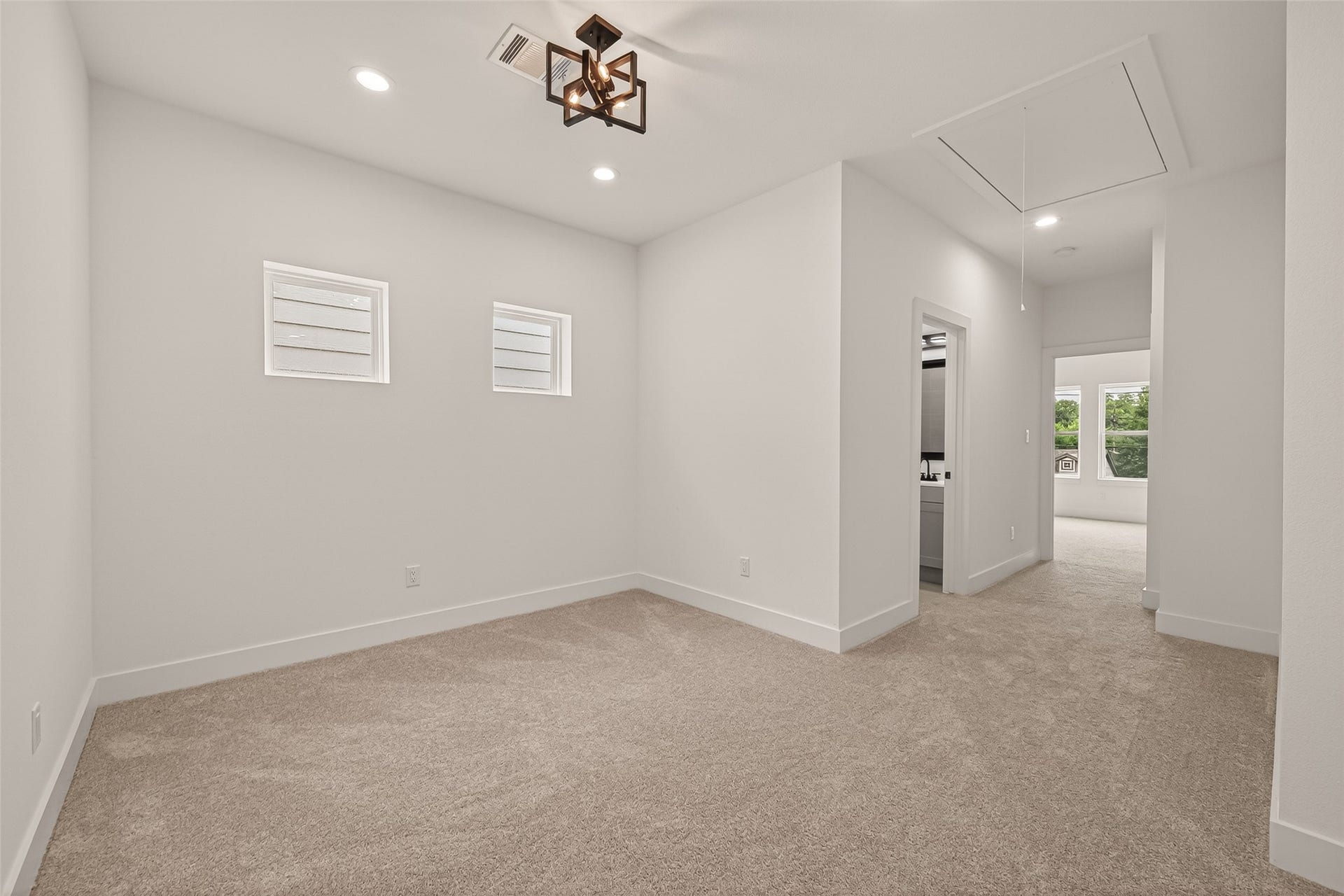 6808 Madrid Street, Houston, TX 77021 This photo shows a bright, carpeted room with modern lighting, featuring two small windows. The room leads to a hallway and has an adjacent space visible, suggesting an open layout.