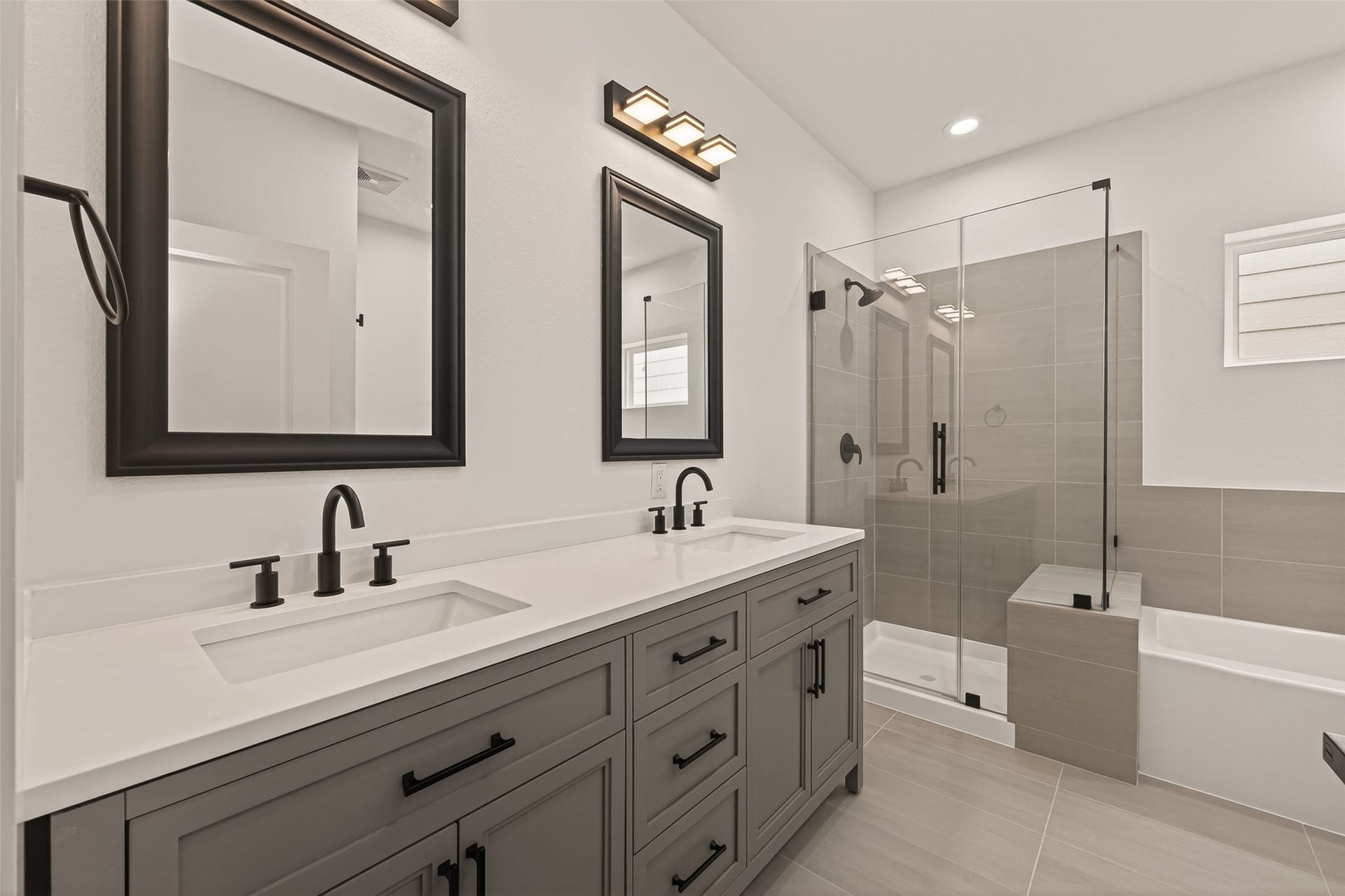 6808 Madrid Street, Houston, TX 77021 This modern bathroom features a sleek double vanity with dark fixtures, large mirrors, and a glass-enclosed shower. The neutral tones and clean lines create a sophisticated and inviting atmosphere.