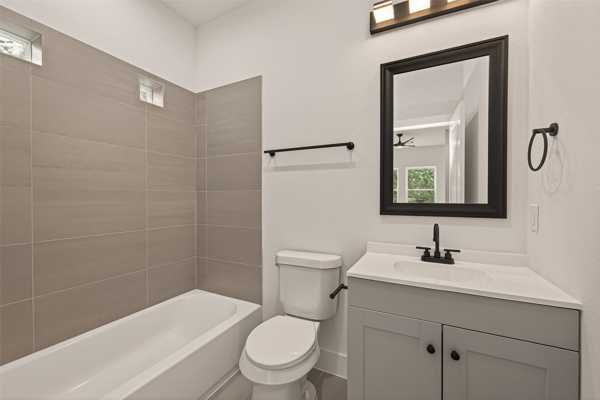 6808 Madrid Street, Houston, TX 77021 This bathroom features a sleek design with neutral tones. It includes a bathtub with modern tile surround, a vanity with a black-framed mirror, and stylish fixtures, creating a clean and inviting space.