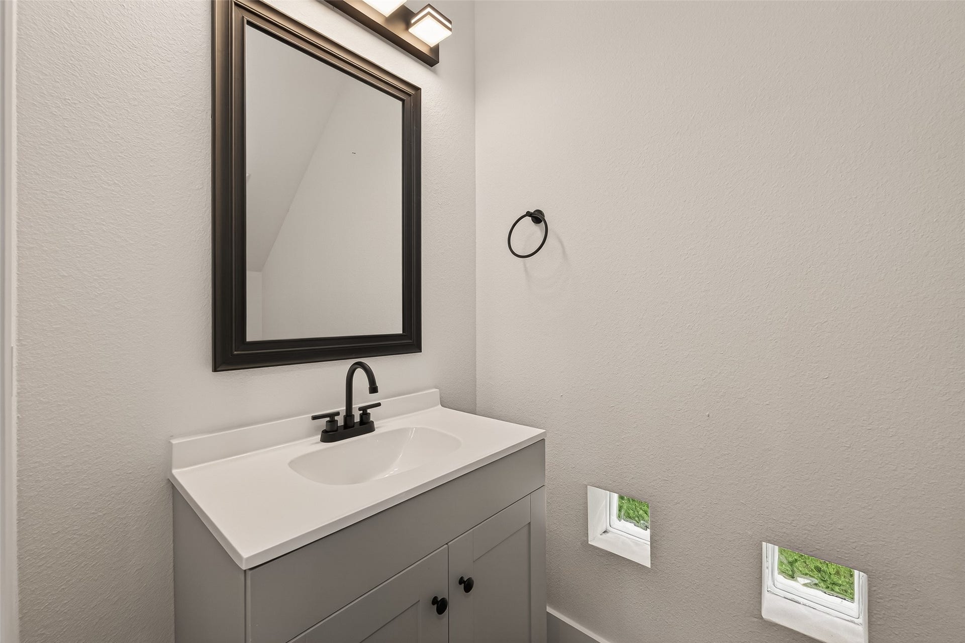 6808 Madrid Street, Houston, TX 77021 This bathroom features a modern vanity with a sleek black faucet and a large framed mirror. The space is well-lit with contemporary lighting, and small windows provide natural light. Neutral tones create a clean and minimalist look.