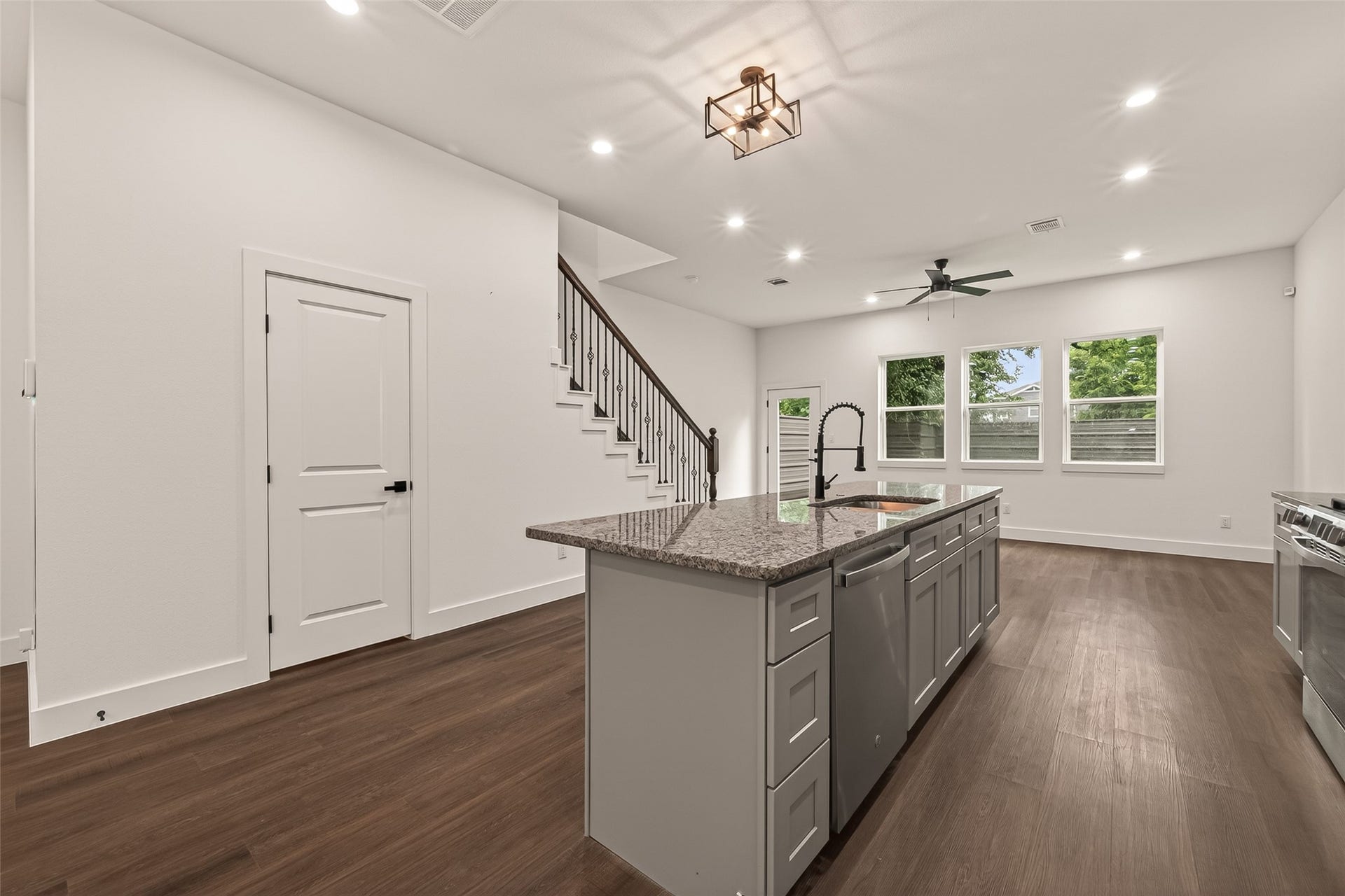 6808 Madrid Street, Houston, TX 77021 This photo showcases a modern open-plan kitchen and living area featuring sleek engineer woodfloors, a large island with granite countertops, stainless steel appliances, and recessed lighting. The space is brightened by ample natural light from multiple windows, and there's a contemporary ceiling fan for added comfort.