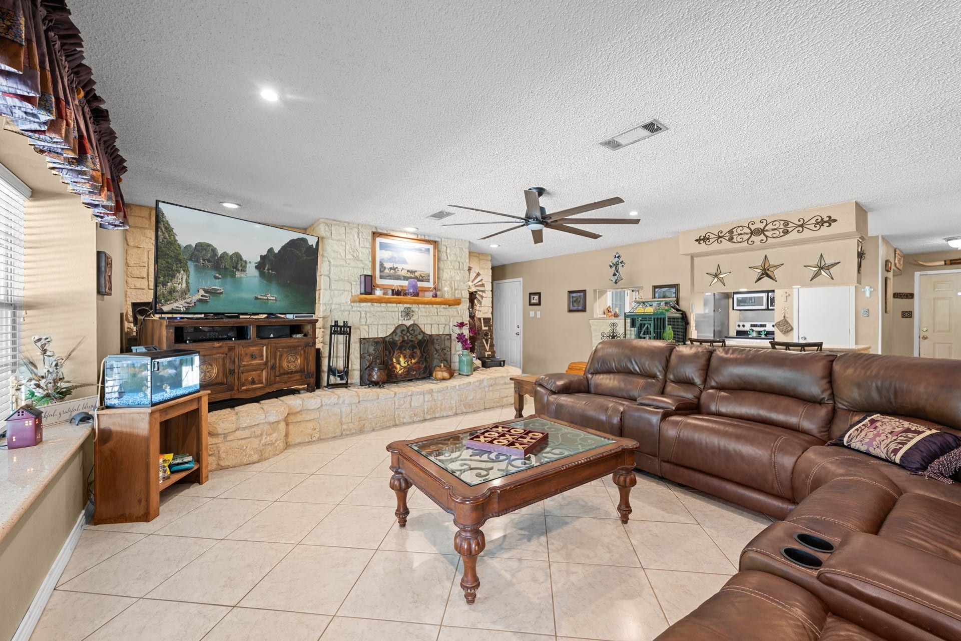 15602 Fir Road, Santa Fe, TX 77517 Inviting open-concept living area centered around a stunning floor-to-ceiling stone fireplace and expansive seating space. Recessed lighting, oversized windows, and seamless flow into the kitchen create an ideal environment for entertaining and everyday comfort.