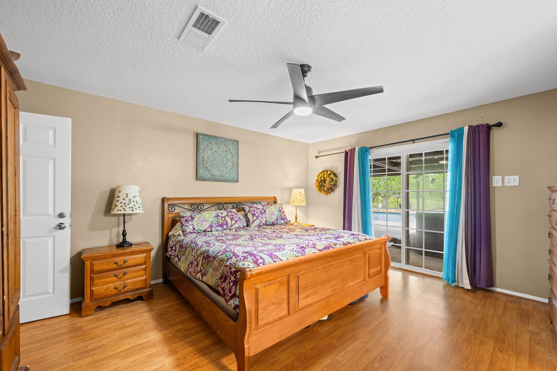 15602 Fir Road, Santa Fe, TX 77517 Spacious primary bedroom featuring warm wood-look flooring, a modern ceiling fan, and abundant natural light. Sliding glass doors provide easy access to the outdoor living area while enhancing the rooms bright and airy feel.