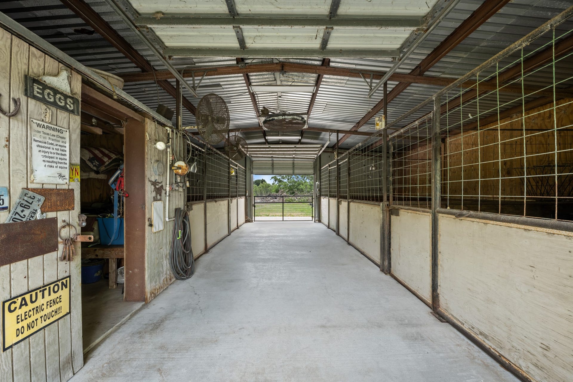 15602 Fir Road, Santa Fe, TX 77517 Well-equipped horse barn interior featuring multiple stalls, wide center aisle access, concrete flooring, and dedicated storage space for tack and equipment. Designed for convenient daily care and efficient ranch functionality.