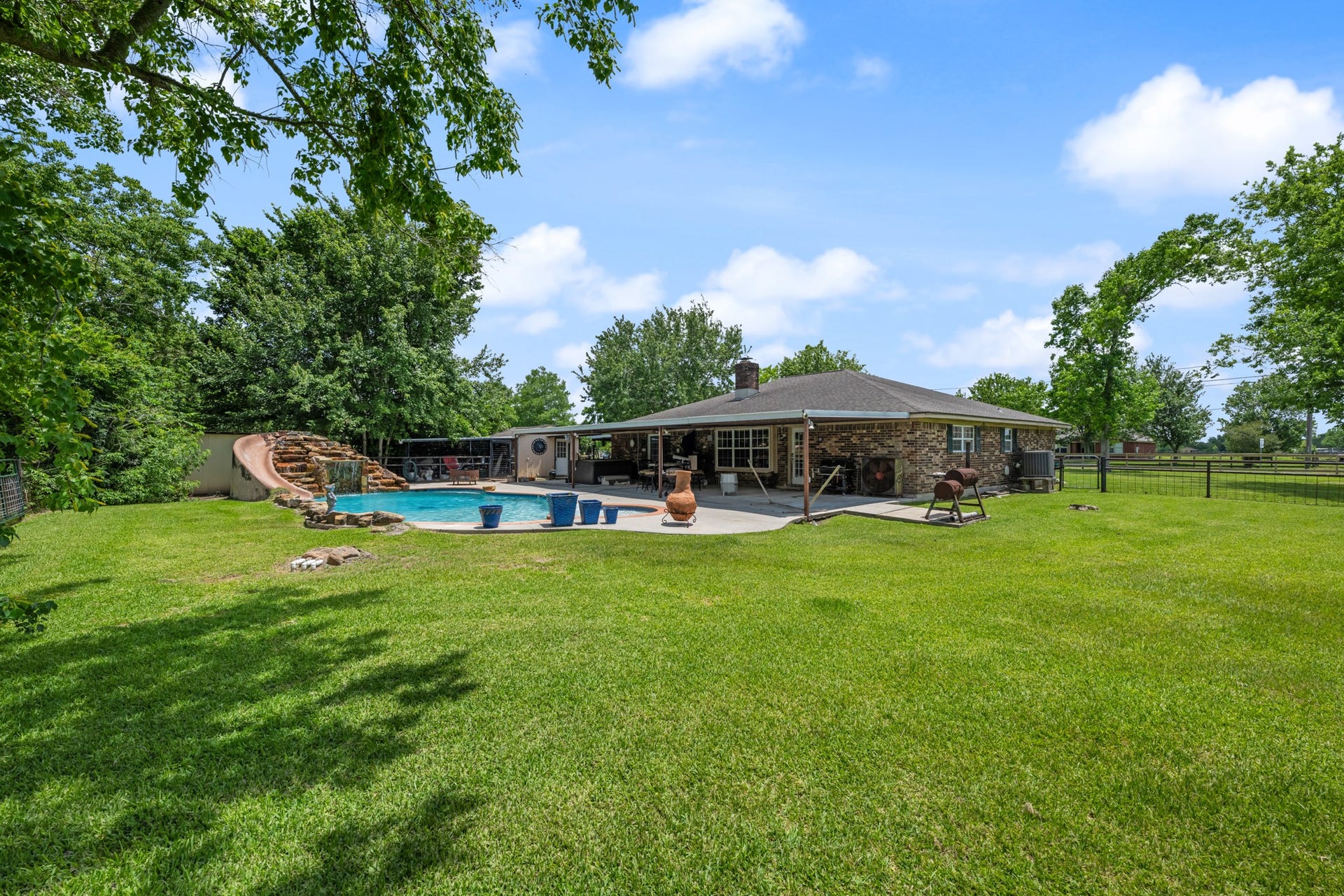 15602 Fir Road, Santa Fe, TX 77517 Expansive backyard retreat featuring a resort-style pool with rock waterfall slide, large covered patio, and plenty of open green space to enjoy. Mature trees and fenced surroundings create a private setting ideal for entertaining, recreation, or relaxing outdoors.