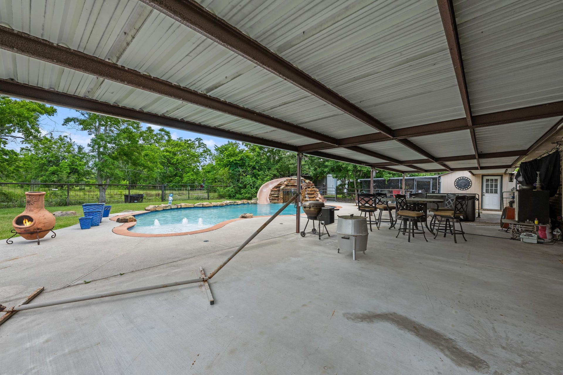 15602 Fir Road, Santa Fe, TX 77517 Resort-style backyard featuring a sparkling pool with rock waterfall slide, expansive covered patio, and multiple seating areas designed for outdoor entertaining. The spacious setup offers the perfect blend of relaxation, recreation, and year-round enjoyment.