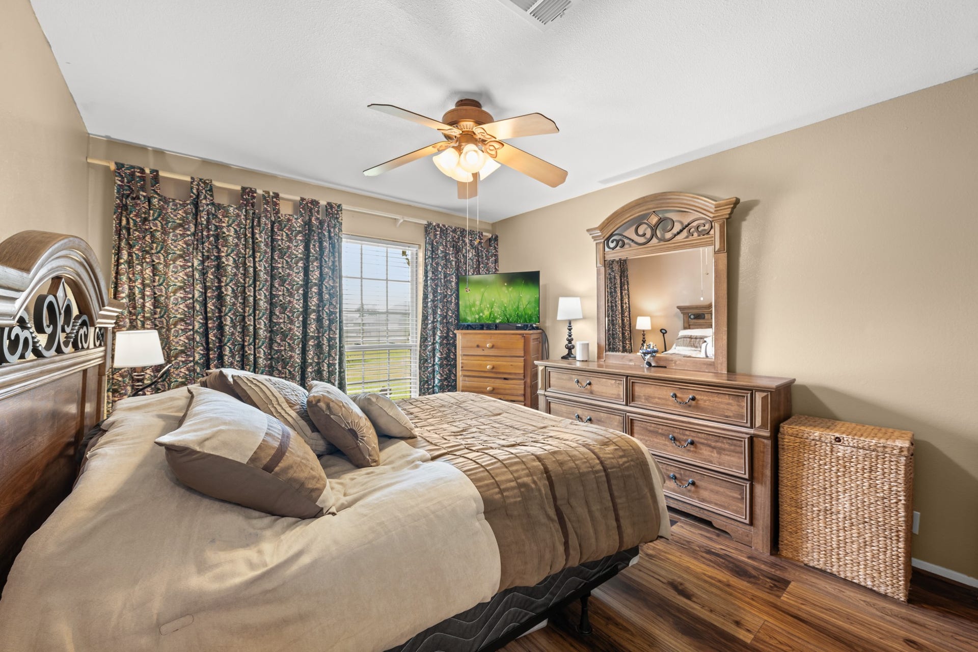 15602 Fir Road, Santa Fe, TX 77517 Comfortable bedroom featuring warm wood-look flooring, neutral tones, and large windows that fill the space with natural light. Generous room size and ceiling fan create a relaxing retreat with plenty of everyday comfort.
