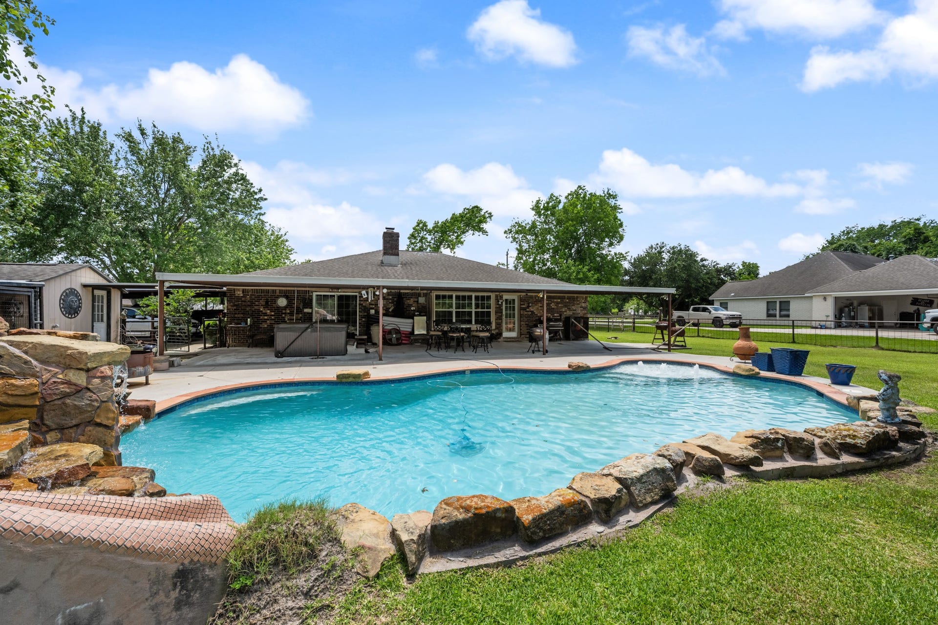 15602 Fir Road, Santa Fe, TX 77517 Spacious backyard oasis featuring a resort-style pool with a custom rock waterfall slide, expansive green space, and a large covered patio perfect for outdoor entertaining and relaxing year-round.