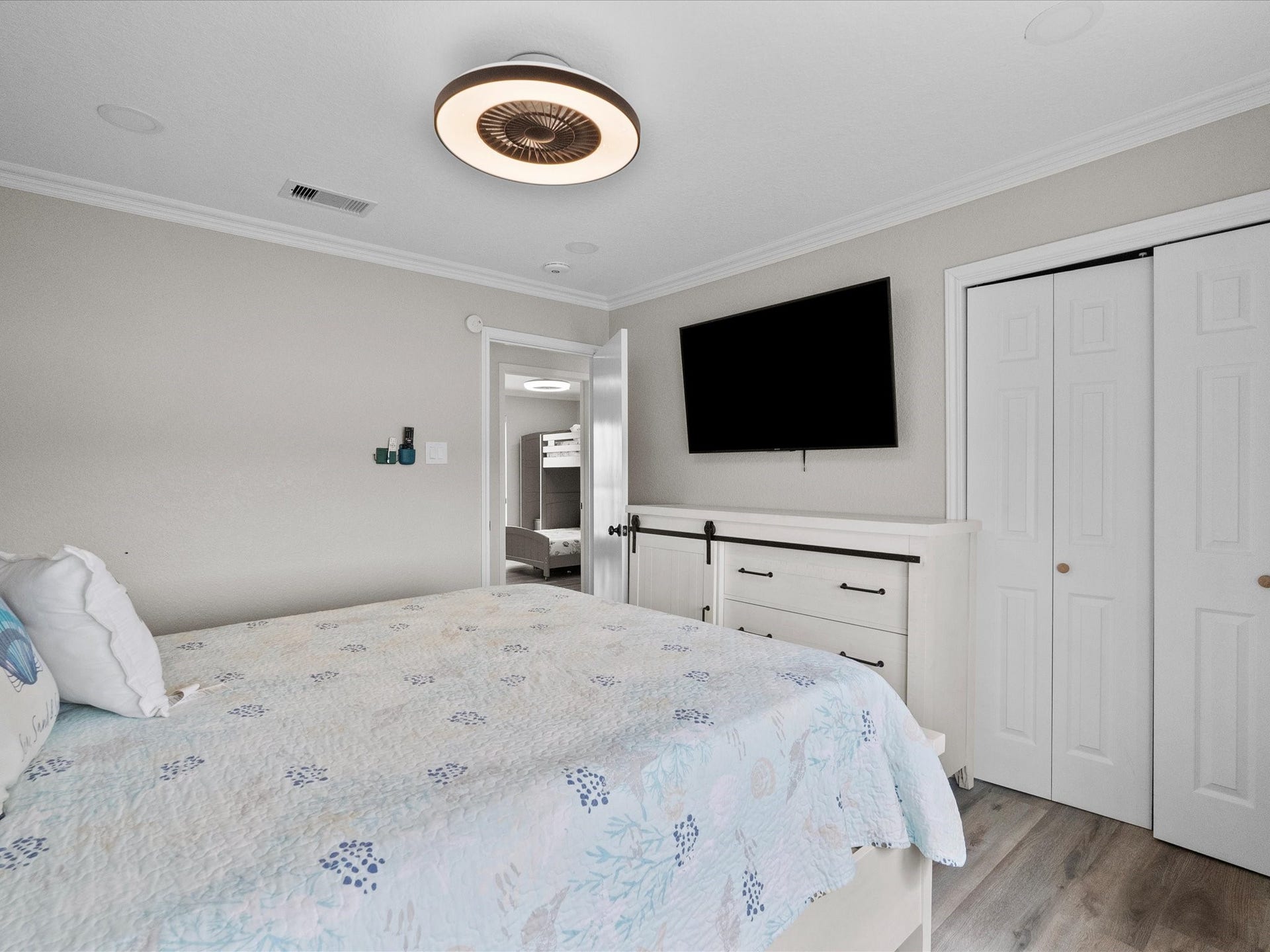 319 Francis Cove, Surfside Beach, TX 77541 A cozy bedroom featuring a soft color palette with light walls and wood flooring. It includes a stylish ceiling fan, mounted TV, and a dresser. The space is bright and welcoming, with a neatly made bed and access to a secondary room.