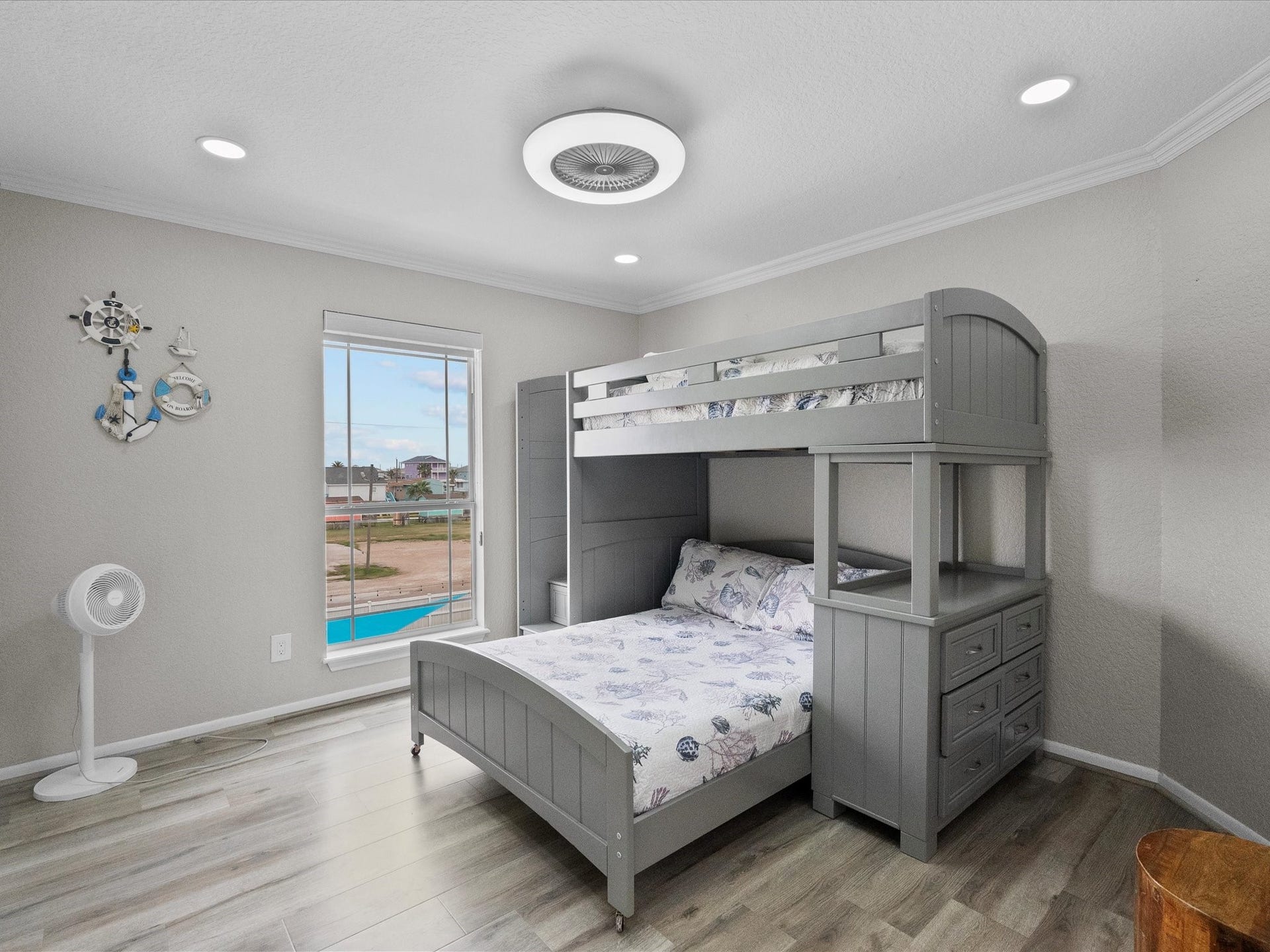 319 Francis Cove, Surfside Beach, TX 77541 This cozy bedroom features a stylish bunk bed with built-in storage, modern recessed lighting, and a ceiling fan. The room offers a view of a pool through a large window, enhancing its bright and airy feel. Nautical-themed decor adds a playful touch.