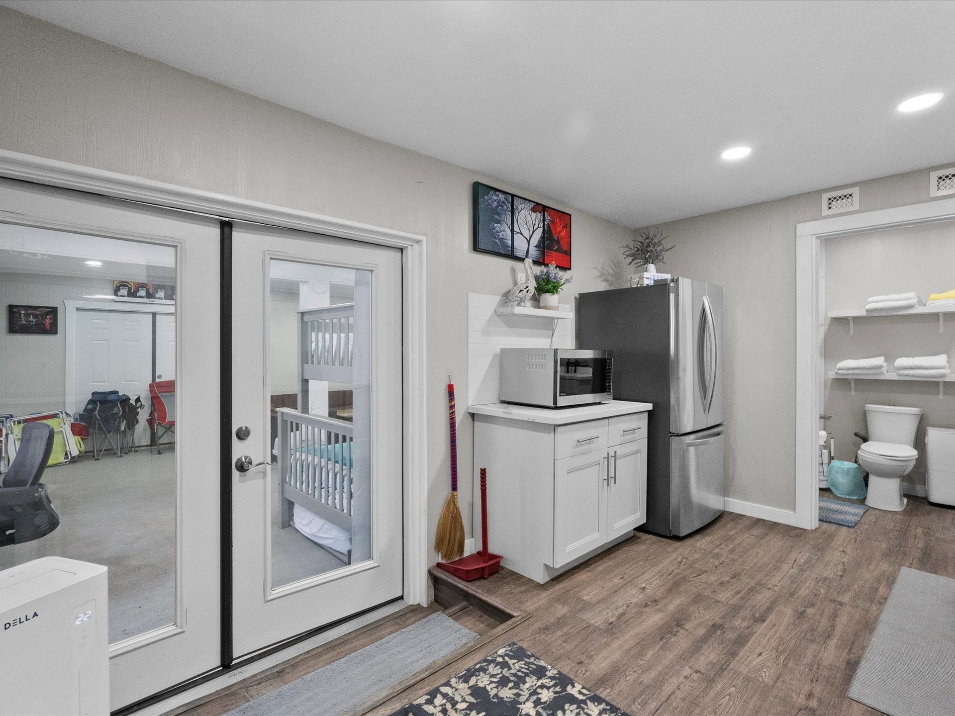 319 Francis Cove, Surfside Beach, TX 77541 This photo showcases a multi-purpose basement area with wood flooring, featuring a kitchenette with modern appliances, and a visible bathroom with open shelving. French doors lead to an adjacent room, enhancing the space's functionality and flow.