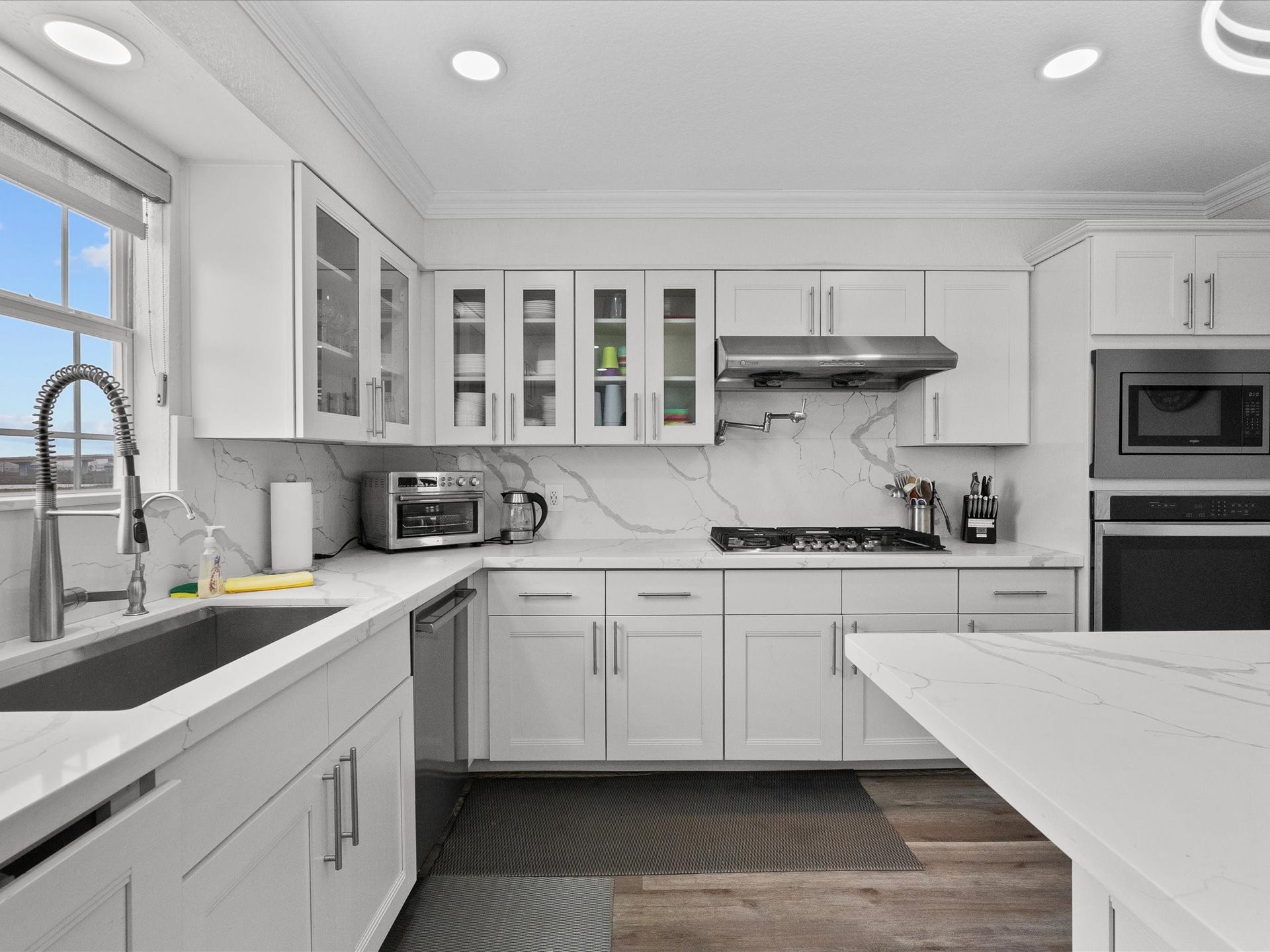 319 Francis Cove, Surfside Beach, TX 77541 The kitchen features a modern design with white cabinetry, marble-patterned countertops, and a sleek backsplash. It includes stainless steel appliances, a gas cooktop, and ample natural light from a large window. Perfect for culinary enthusiasts.