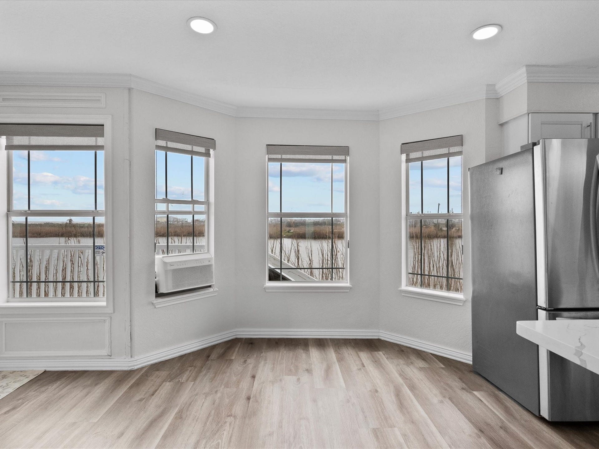 319 Francis Cove, Surfside Beach, TX 77541 Bright room with large windows offering scenic views, featuring light wood flooring and a modern stainless steel refrigerator. Perfect for enjoying natural light and open space.