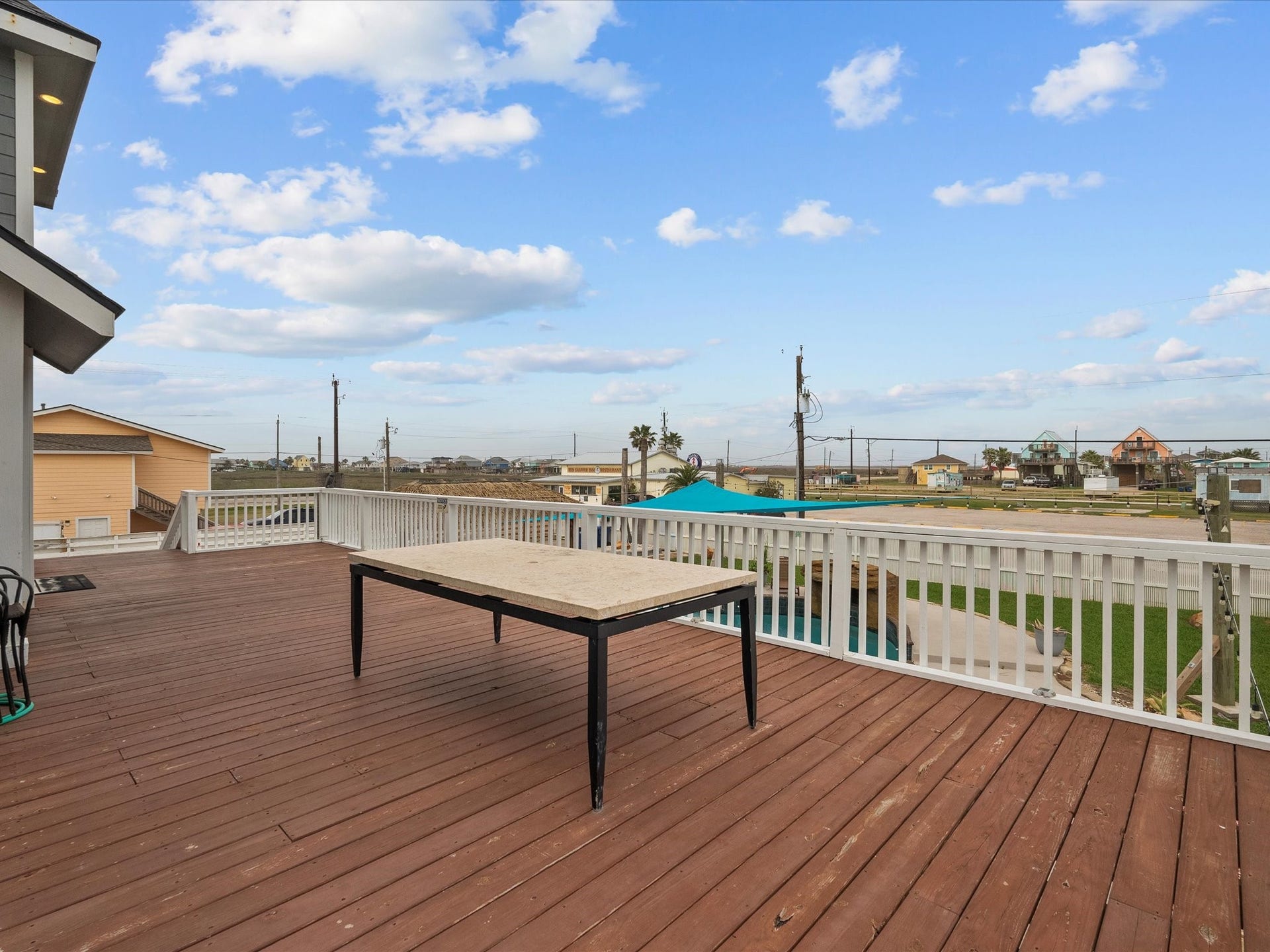 319 Francis Cove, Surfside Beach, TX 77541 This photo shows a spacious wooden deck with a simple table and white railing, offering a view of a suburban neighborhood and open skies. Ideal for outdoor relaxation.