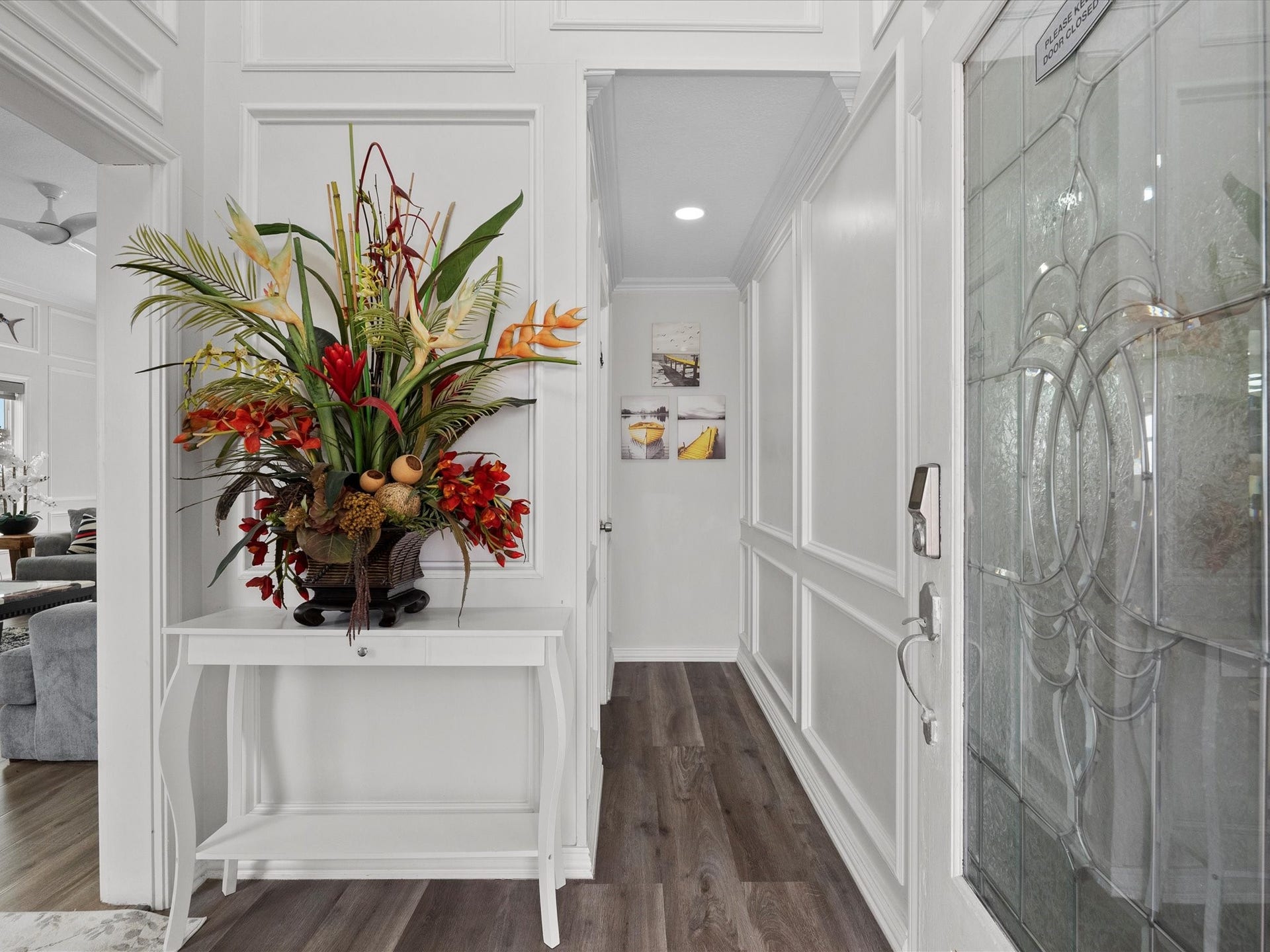 319 Francis Cove, Surfside Beach, TX 77541 Elegant entryway with decorative paneling, a glass front door, and a stylish floral arrangement on a table, leading to a cozy living space with wood flooring.