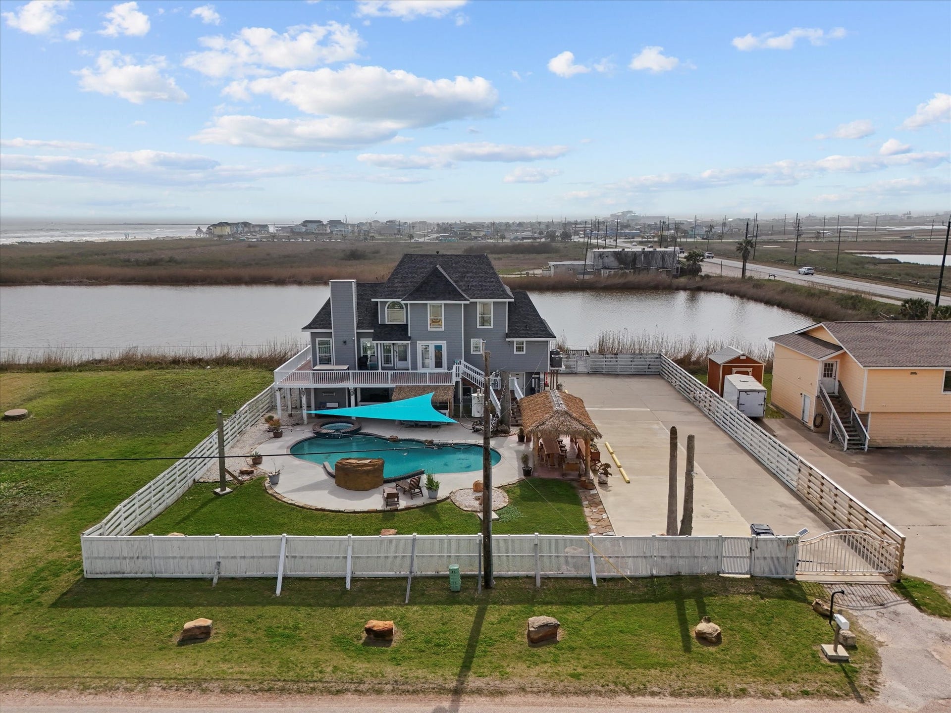319 Francis Cove, Surfside Beach, TX 77541 This waterfront property features a spacious two-story home with a large backyard, including a pool, patio, and covered seating area. The surrounding landscape offers scenic views of the water and open skies, providing a serene and private setting.