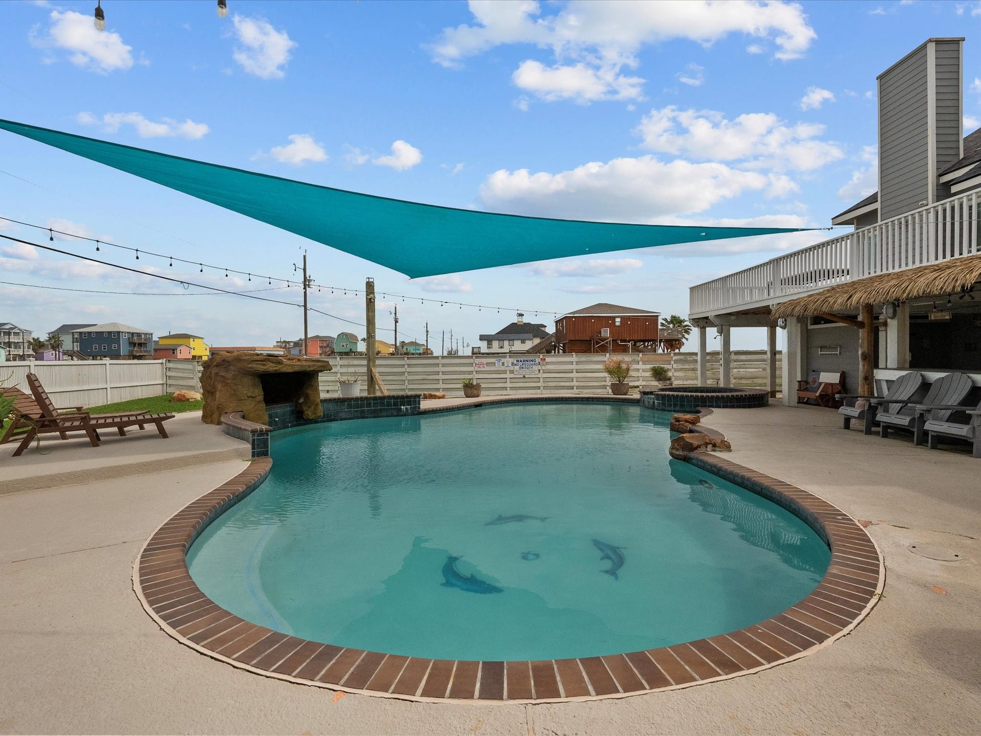 319 Francis Cove, Surfside Beach, TX 77541 This front yard features a stylish pool with a brick border, a rock waterfall, and a shaded sail canopy. Surrounding the pool are lounge chairs and a spacious patio area, perfect for relaxation and outdoor gatherings.