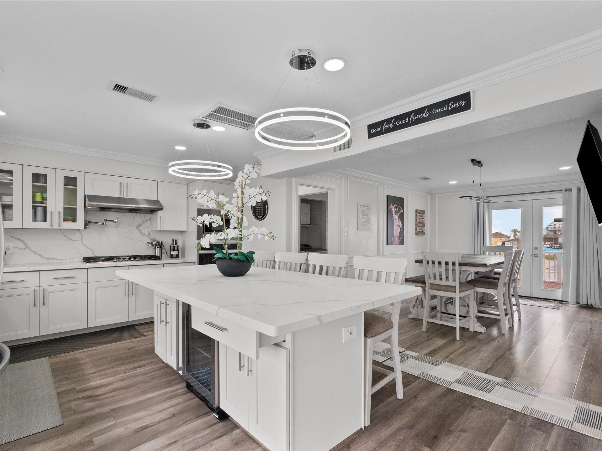 319 Francis Cove, Surfside Beach, TX 77541 This photo showcases the modern, open-concept kitchen and dining area. The kitchen features sleek white cabinetry, stainless steel appliances, and a large island with a marble countertop. Elegant light fixtures and wood flooring add warmth, while large windows offer plenty of natural light. It's a stylish and inviting space perfect for entertaining.
