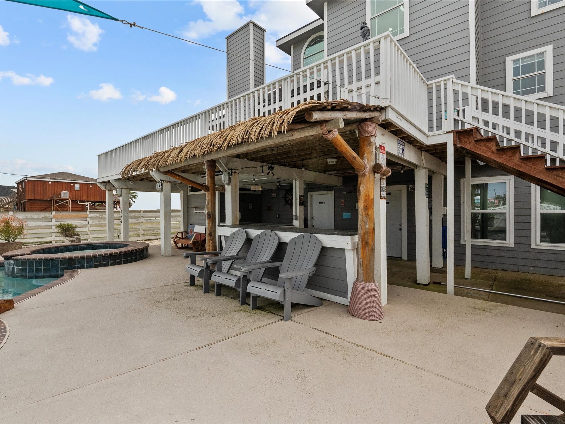 319 Francis Cove, Surfside Beach, TX 77541 This home features a spacious outdoor area with a covered patio and seating, perfect for entertaining. It includes a built-in bar and overlooks a pool, offering a relaxing retreat. The exterior is modern with gray siding and white accents, and there's a convenient staircase leading to the upper level.
